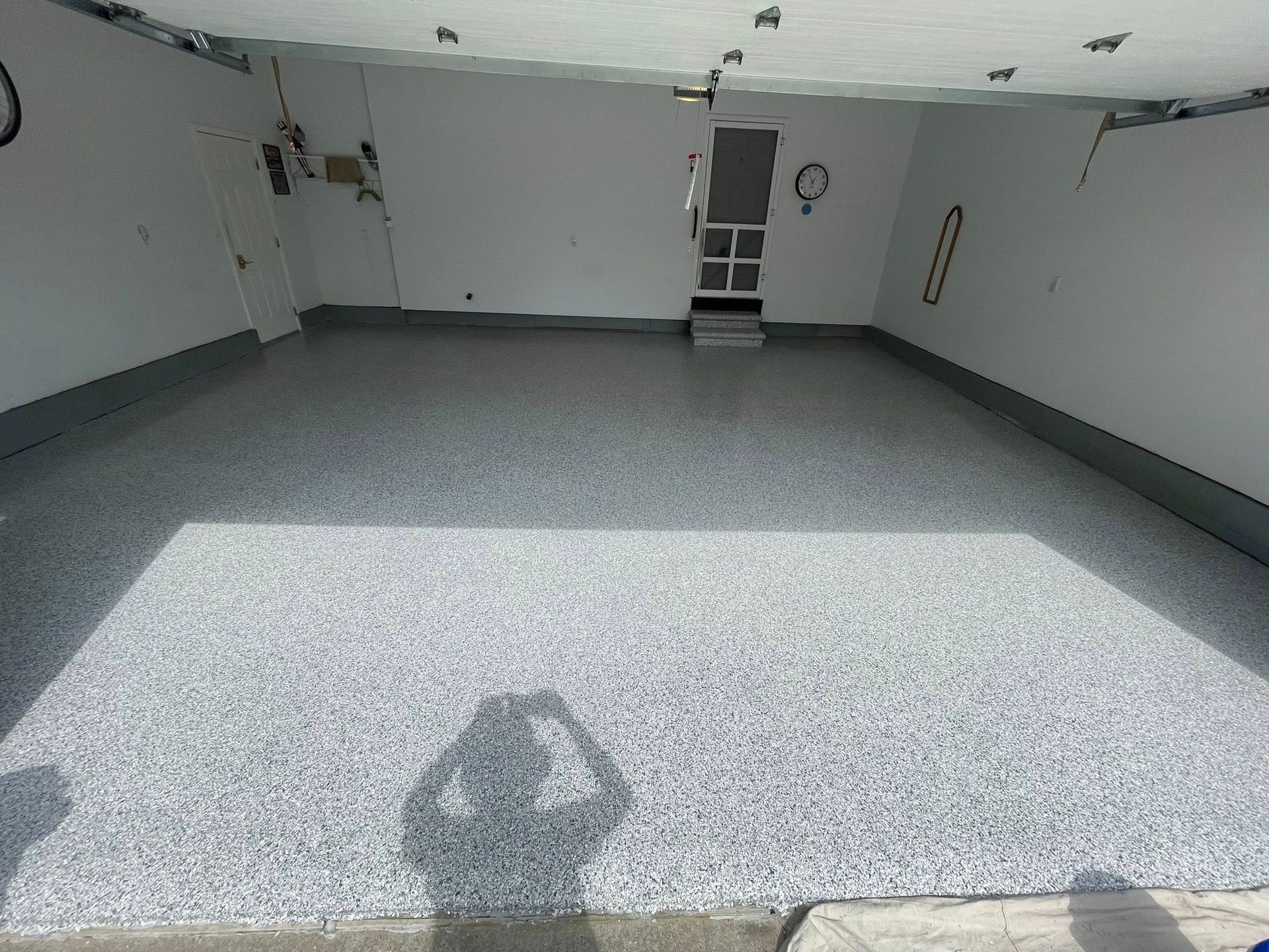 Empty garage with speckled gray epoxy floor. Shadow of person taking photo.