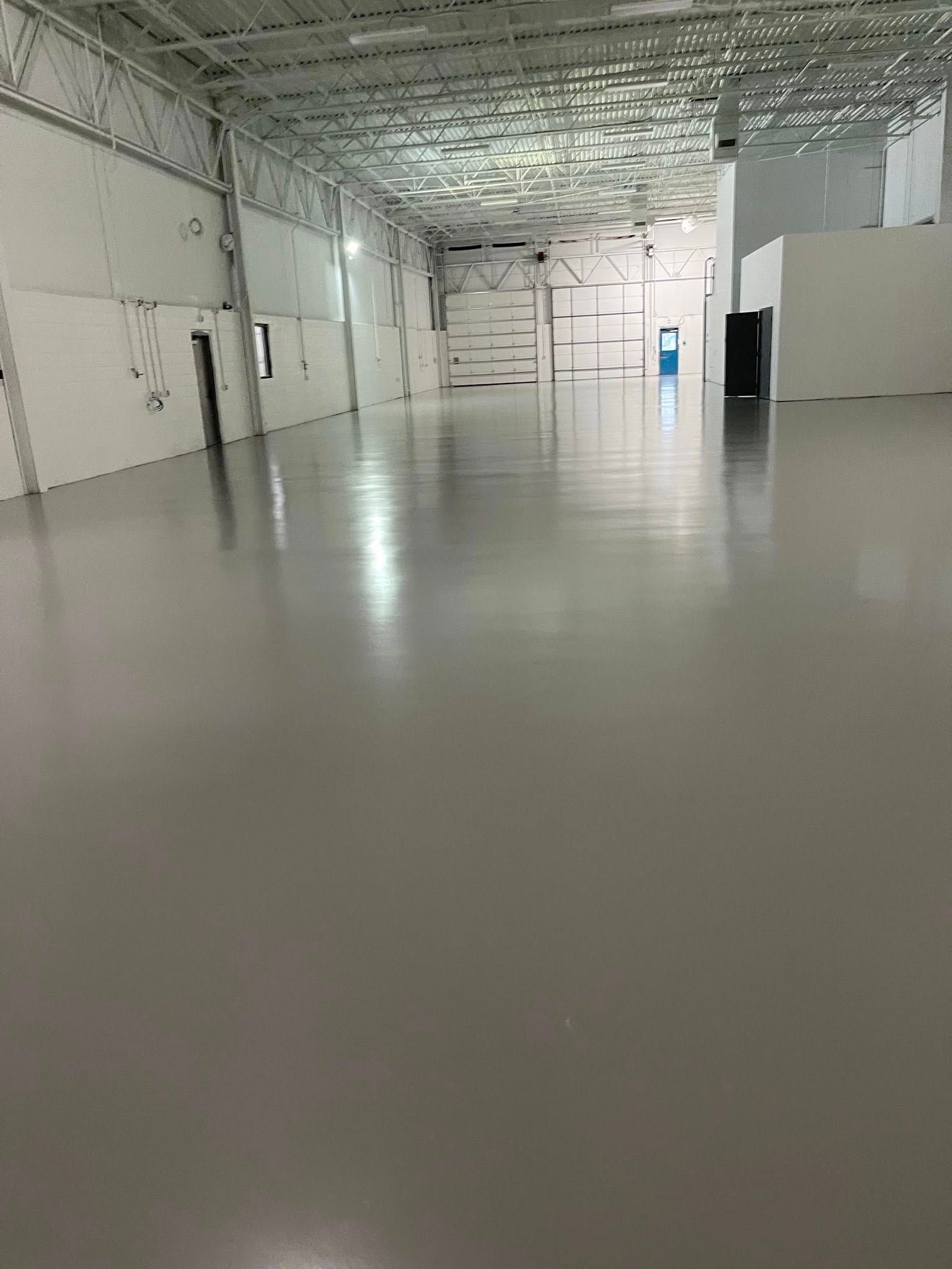 Empty, spacious industrial building with gray floors and white walls, overhead metal beams.