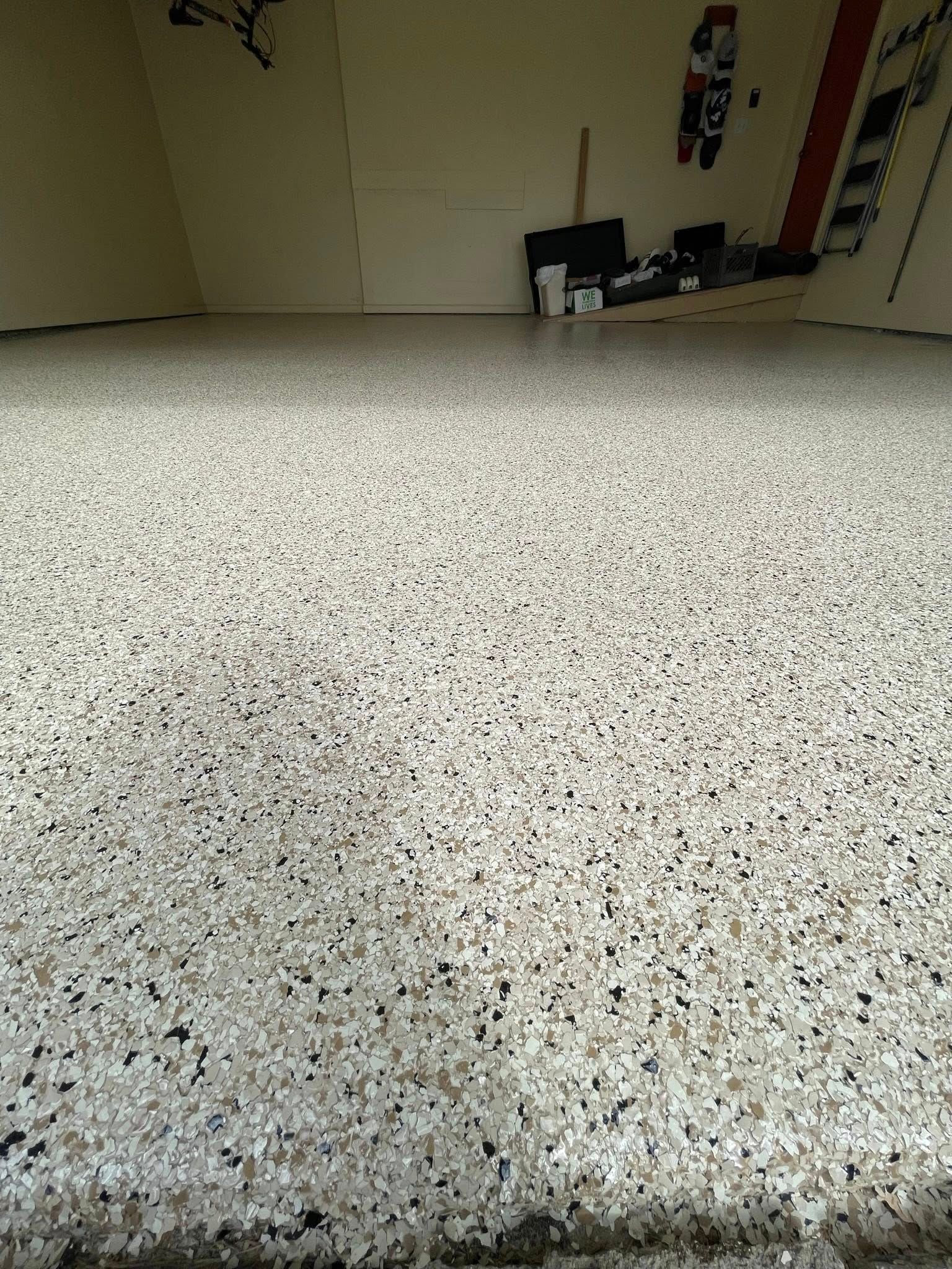 Garage floor with a speckled, light-colored epoxy finish. Tools and equipment sit in the background.