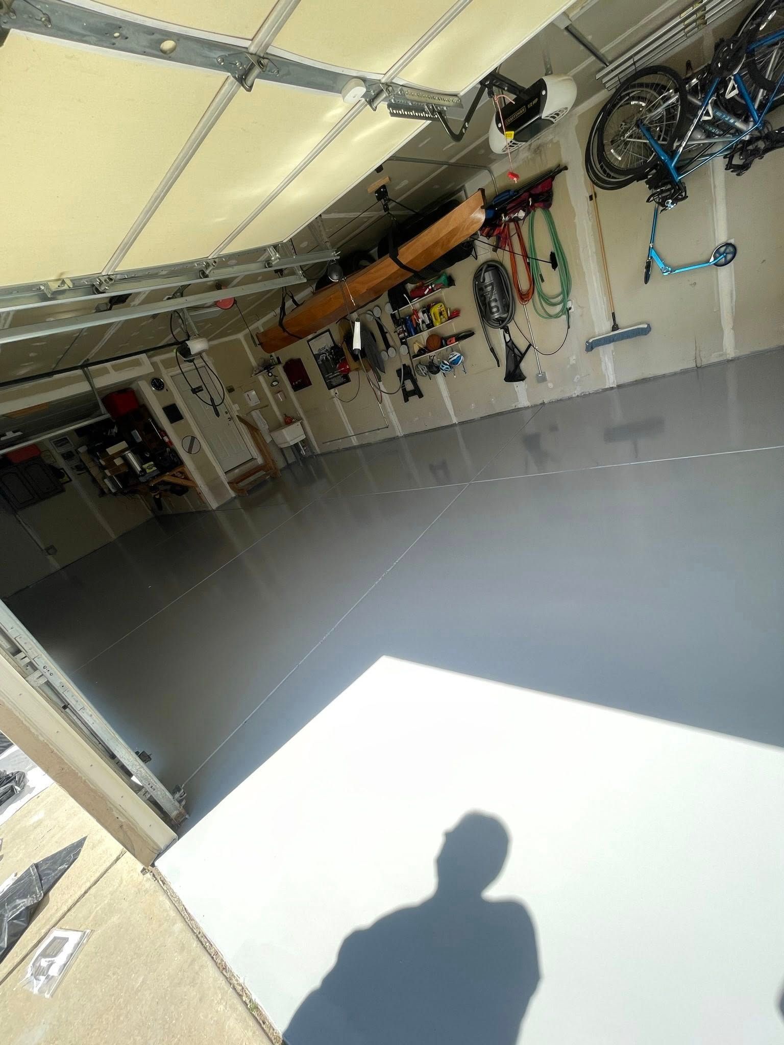 Garage interior with a shiny gray floor, tools on walls, and a shadow in the foreground.