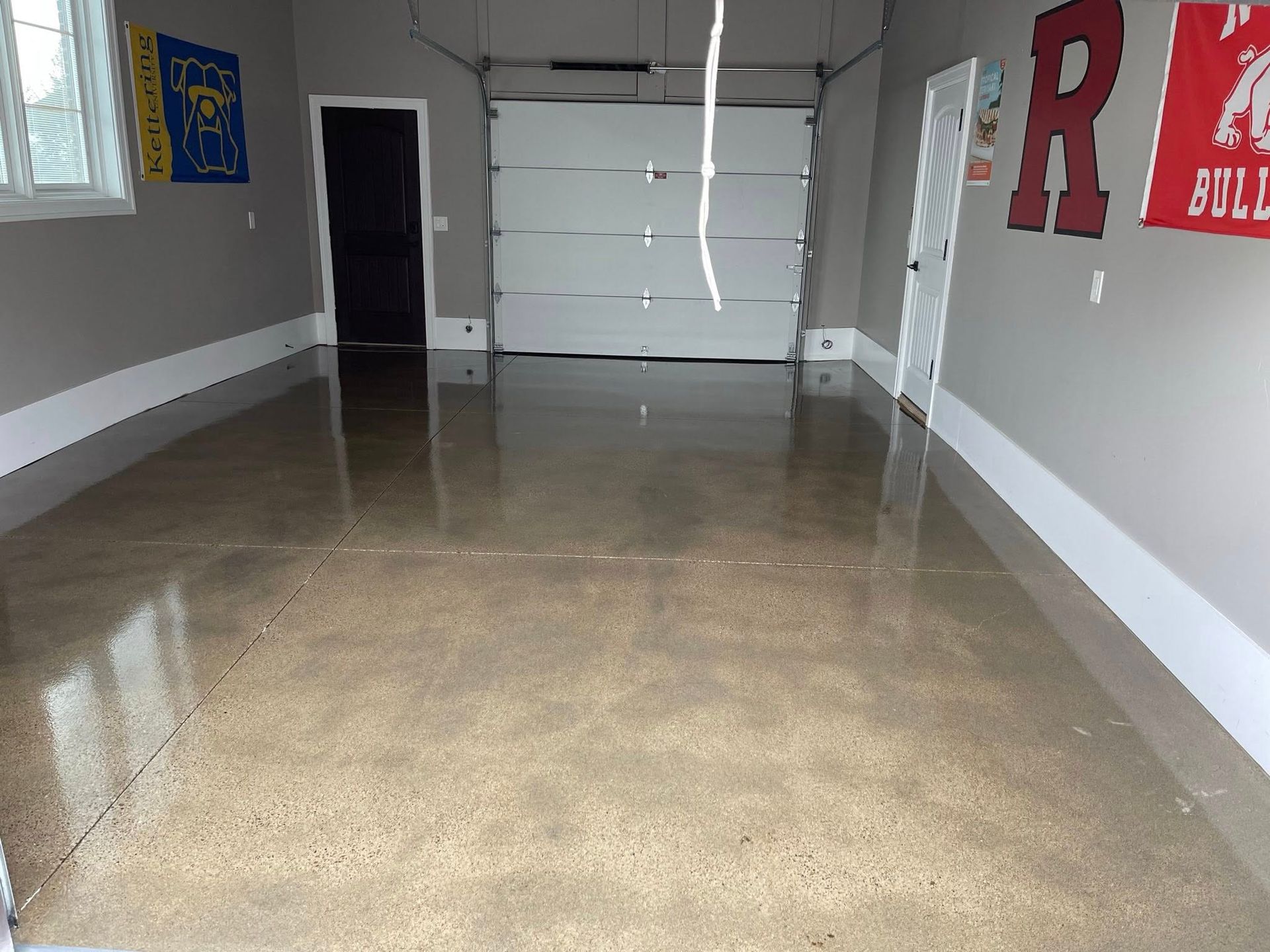 A freshly coated garage floor with gray walls and a white garage door; sports banners on the walls.