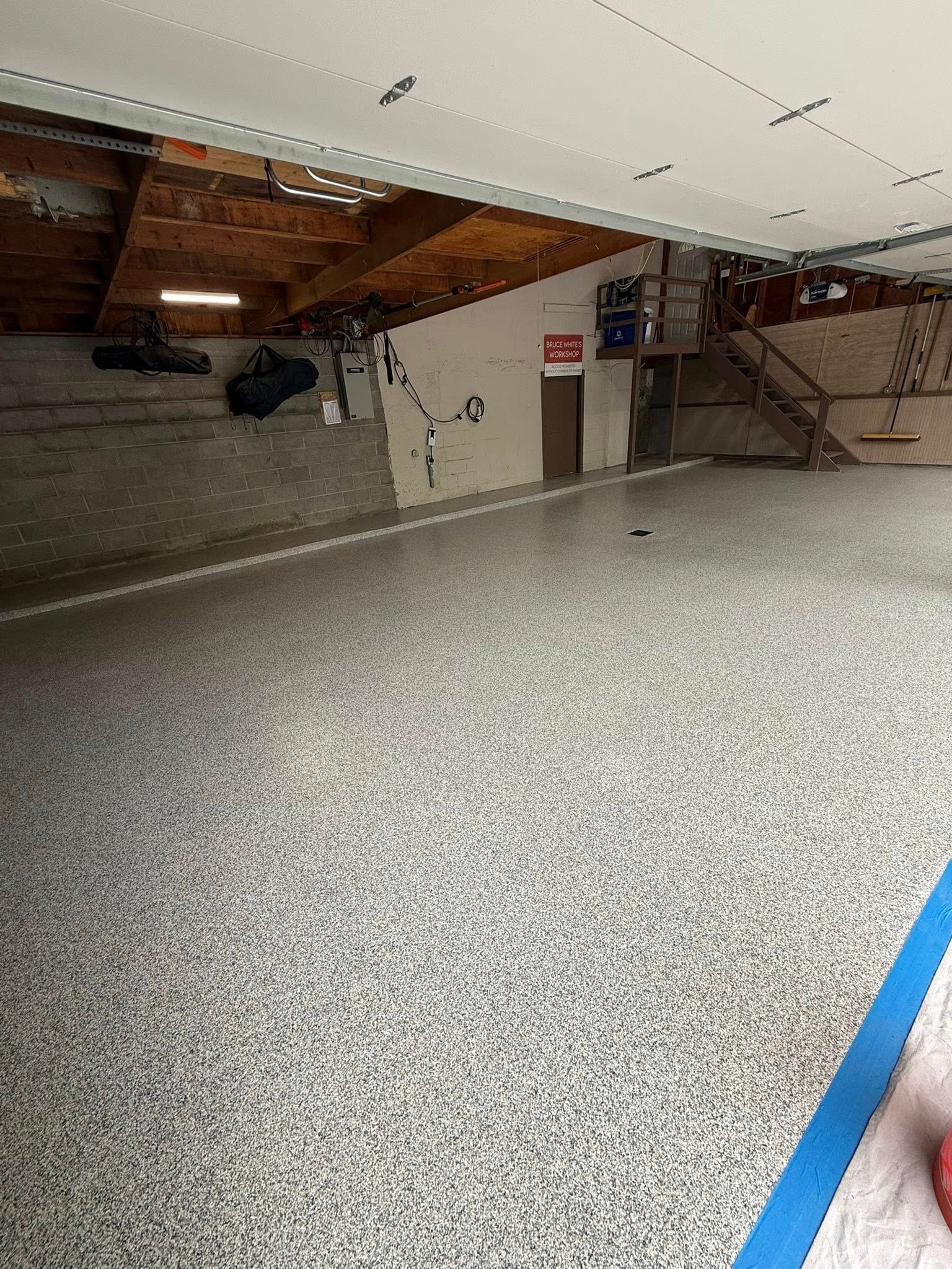 Garage with speckled epoxy floor, exposed beams, and a partially finished wall.