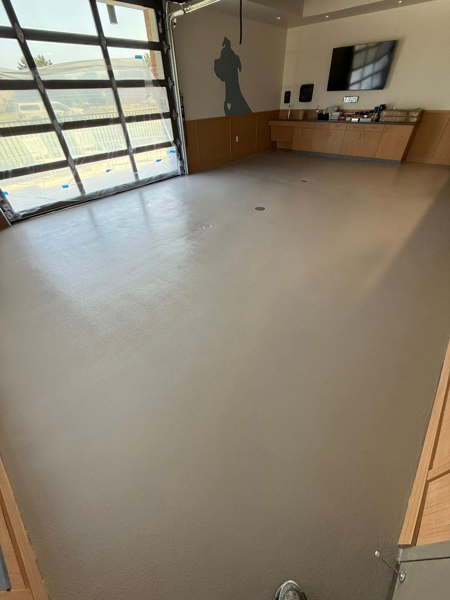 An empty room with a shiny floor, a large window-door, and a television on the wall.