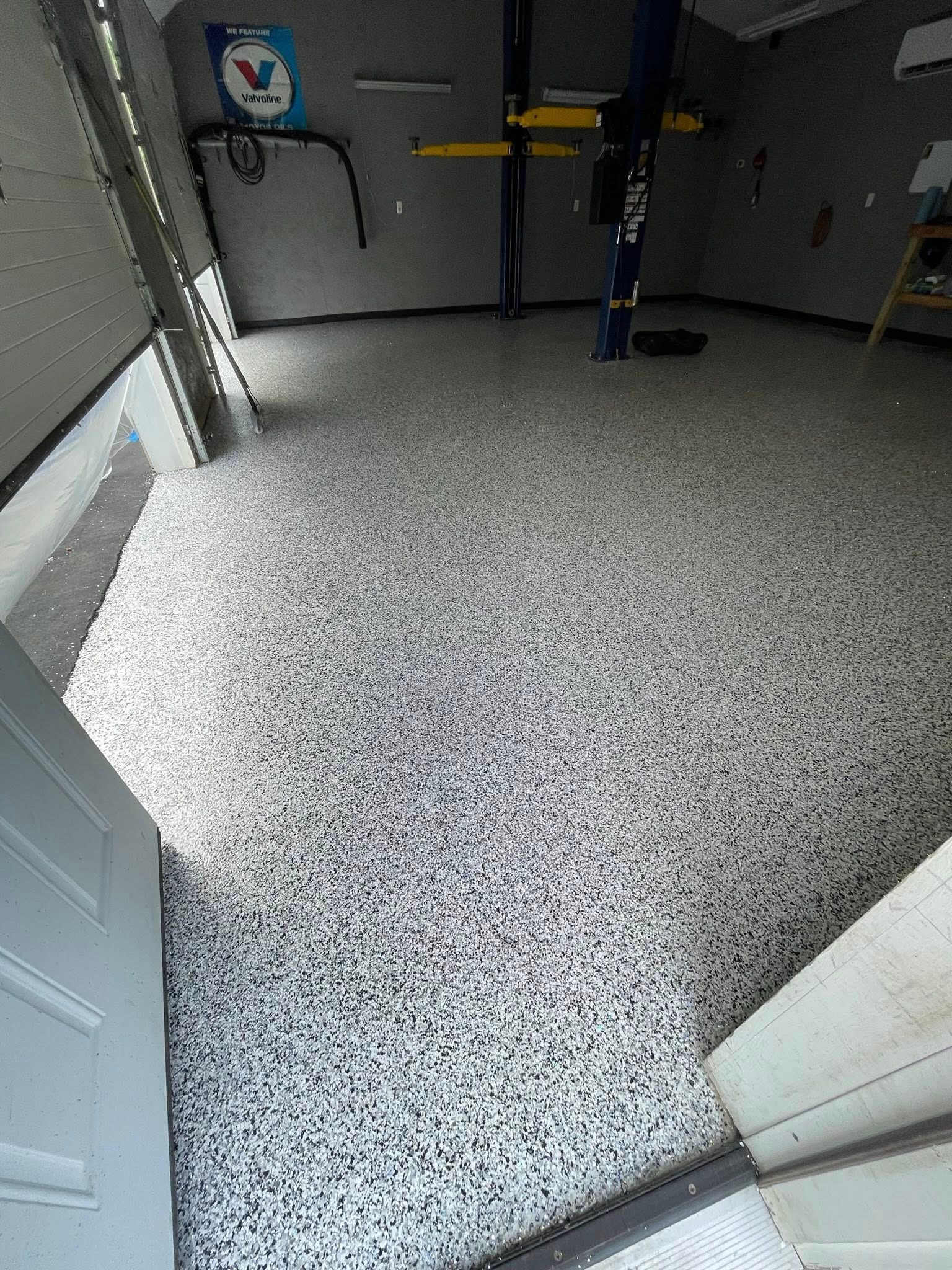 Garage with speckled gray and white epoxy floor. Car lift in the background. Open door in the foreground.