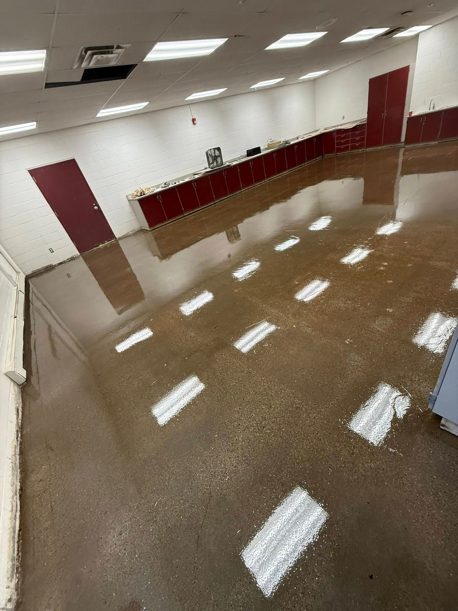 Flooded interior with polished concrete floor, burgundy accents, and overhead fluorescent lights.
