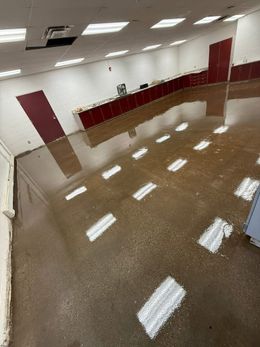Flooded interior room with brown floor reflecting overhead lights and maroon cabinets along the wall.