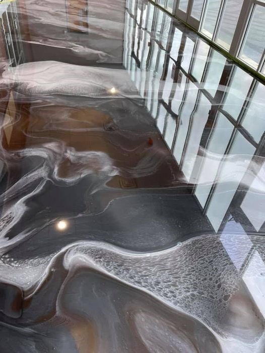 Swirled metallic epoxy floor in shades of gray, white, and brown; reflections of a windowed wall.