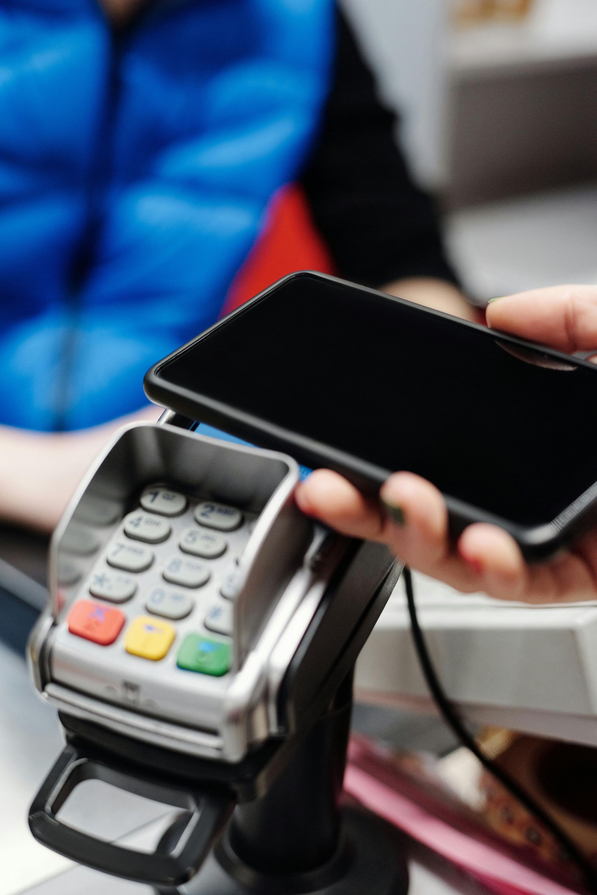 A person is holding a cell phone over a credit card machine.