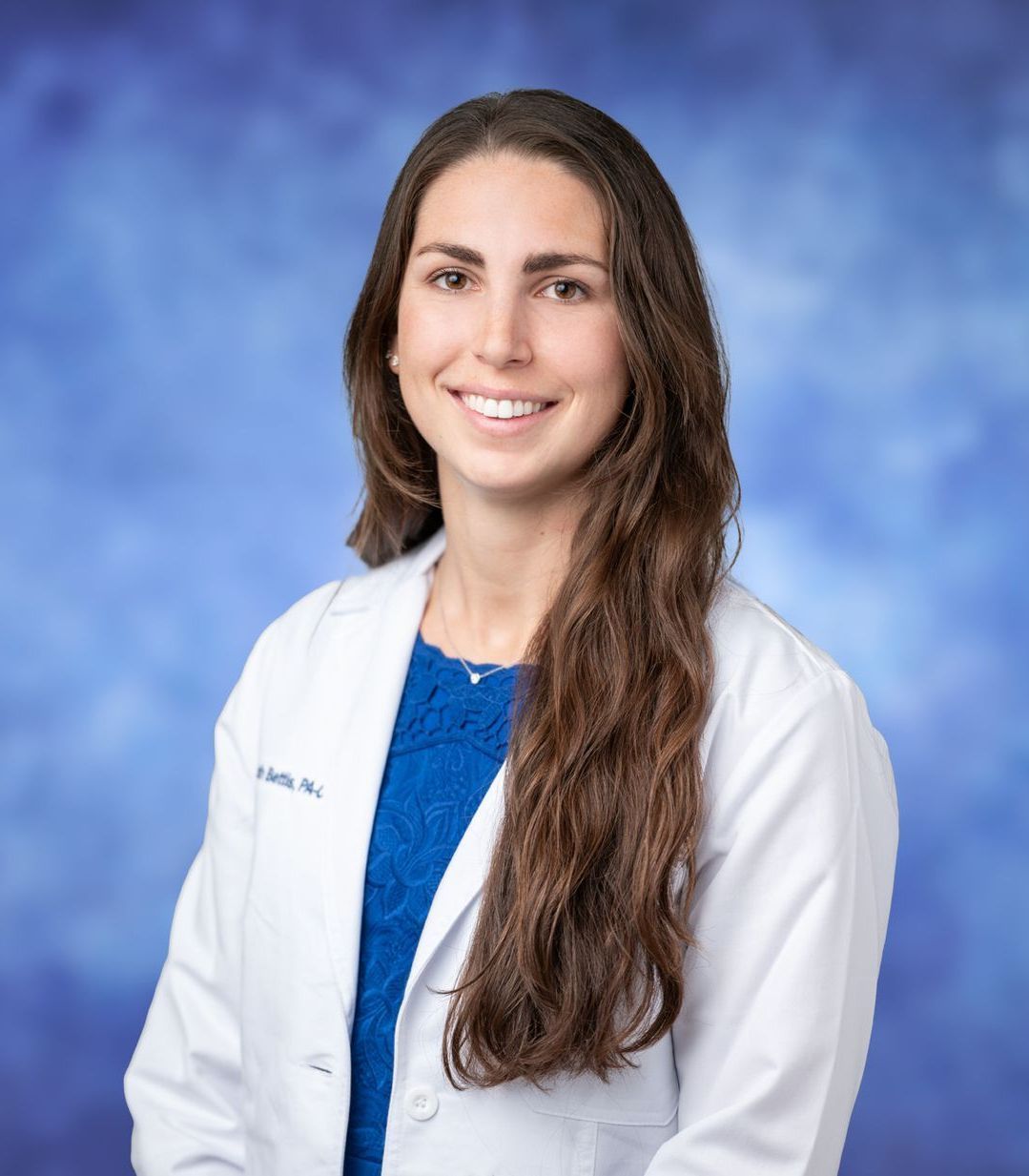 A woman, Elizabeth Bettis, in a white lab coat is smiling in front of a blue background.