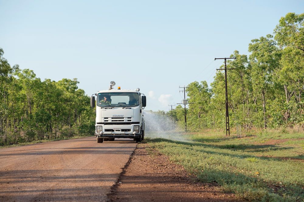 A Yellow Tractor is Driving Down a Dirt Road Next to a Truck — Diggamen Civil Contracting in Tivendale, NT
