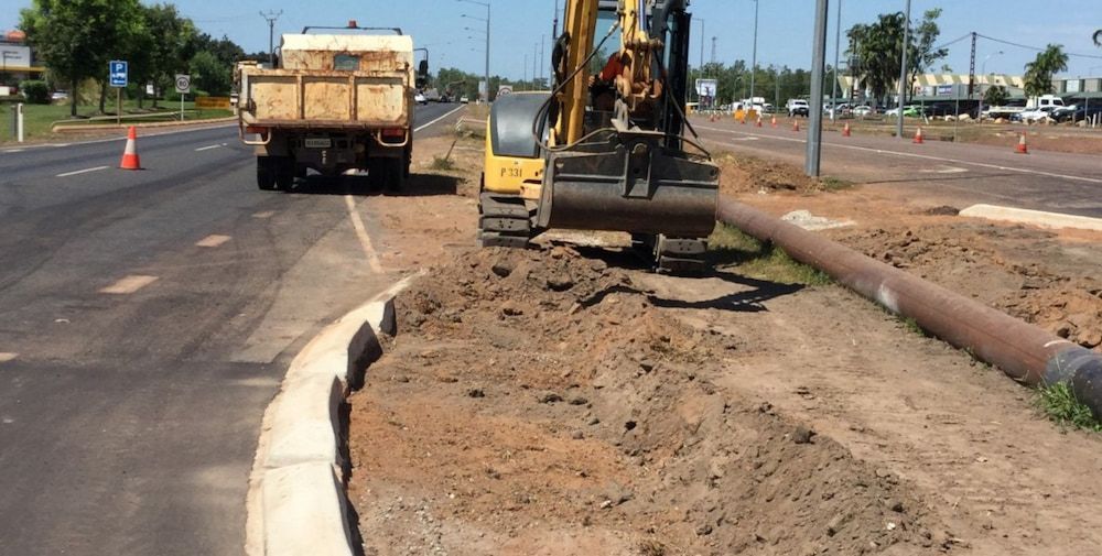 A Yellow Excavator Is Digging in The Dirt Next to A Dump Truck — Diggamen Civil Contracting in Tennant Creek, NT