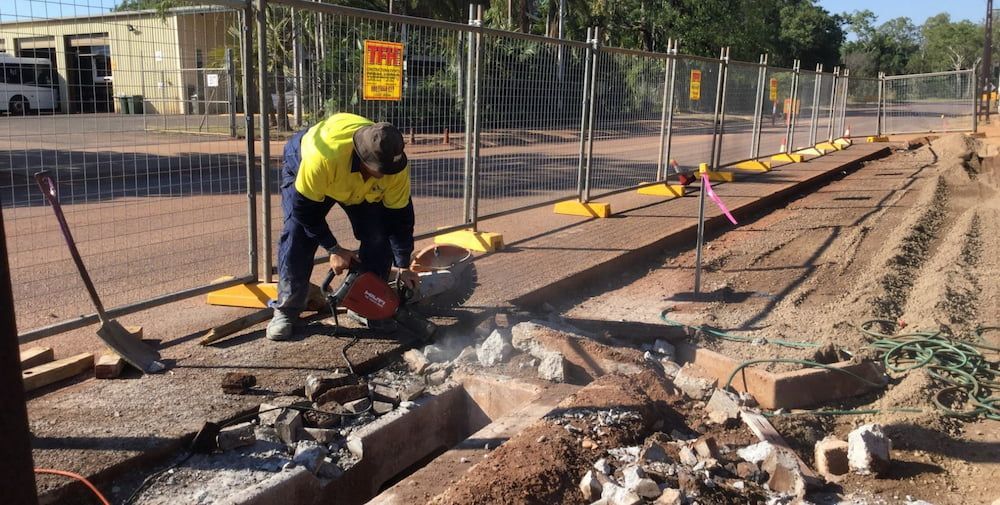 A Man Is Cutting a Hole in The Ground with A Circular Saw — Diggamen Civil Contracting in Palmerston, NT