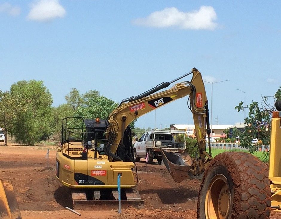 A Cat Excavator Is Digging a Hole in A Dirt Field — Diggamen Civil Contracting in Jabiru, NT