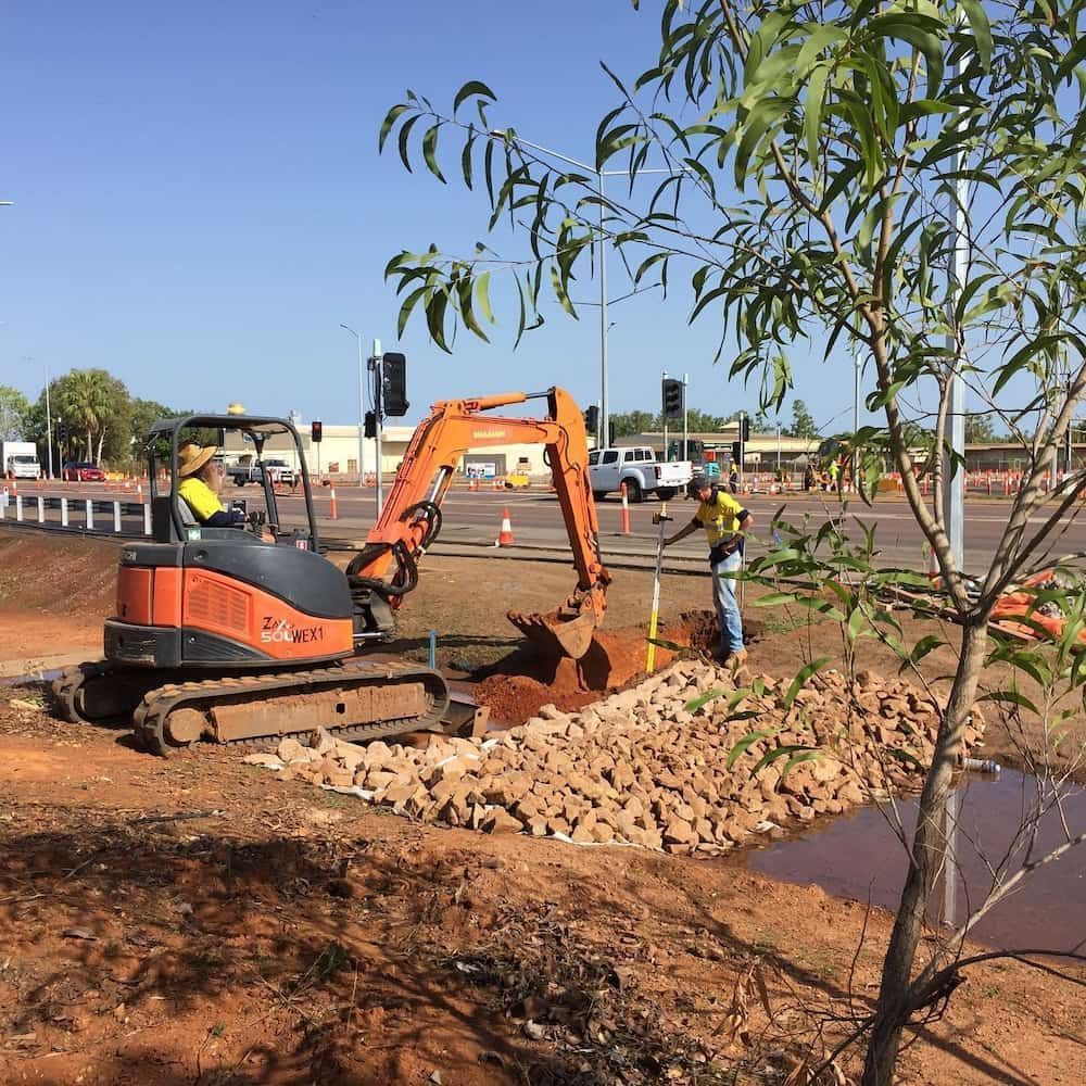An Excavator is Digging a Hole in the Dirt Next to a Tree — Diggamen Civil Contracting in Tivendale, NT