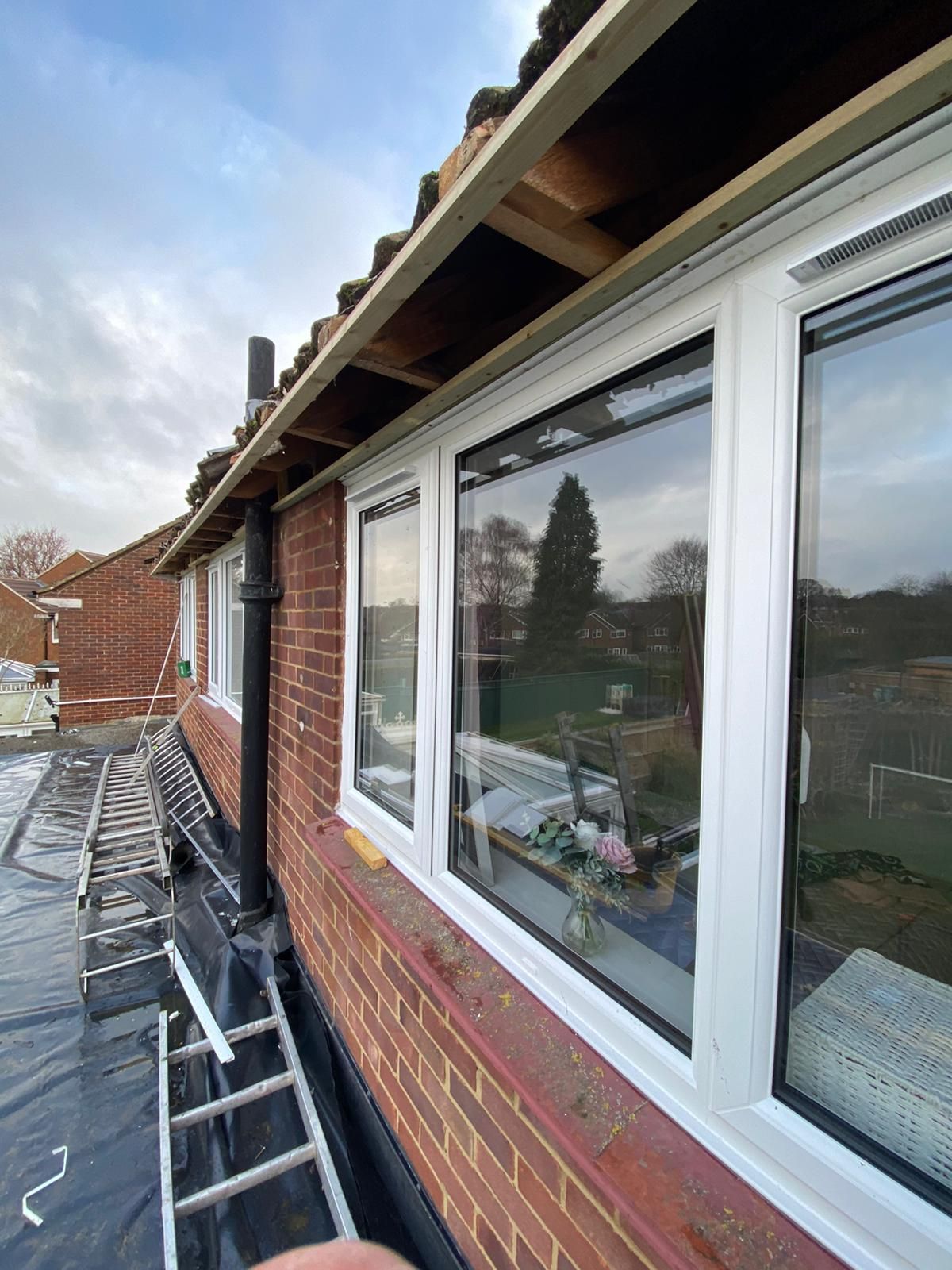 A ladder is sitting on the side of a brick building next to a window.