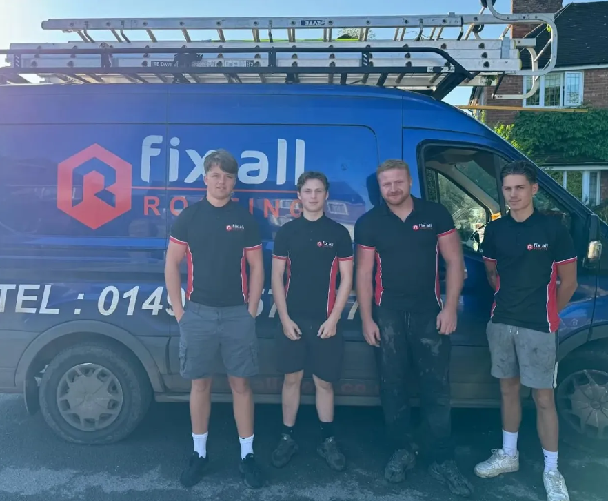 Four people in black shirts stand next to a Fix All Roofing van with a ladder on top.
