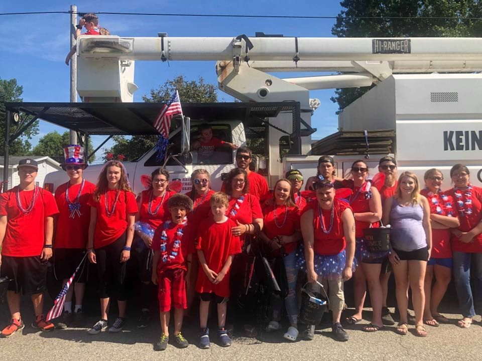 A group of people in red shirts are standing in front of a white truck.