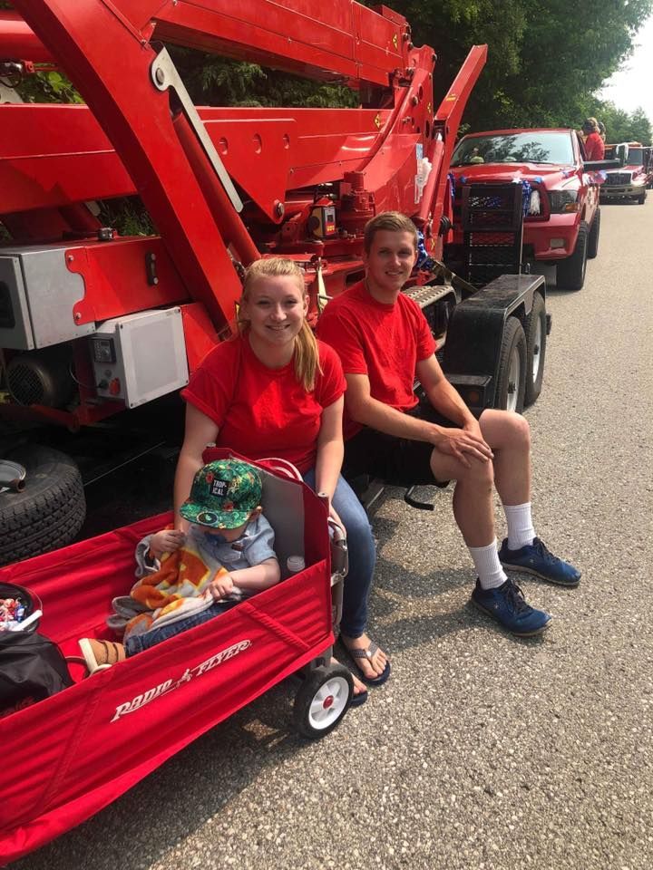 A man and a woman are sitting in a red wagon with a child in it.