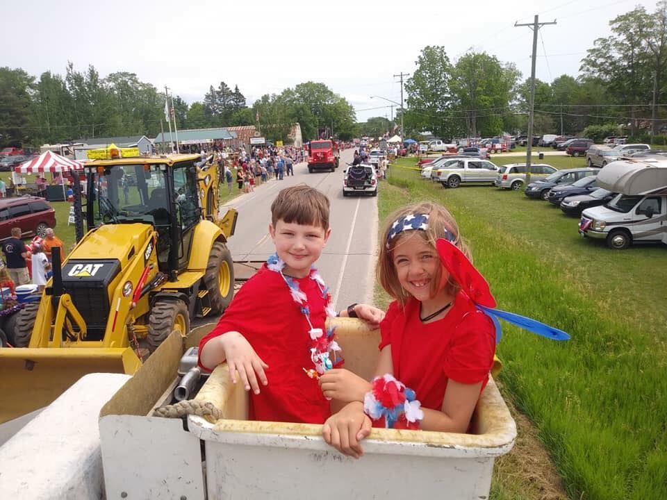 A boy and a girl are sitting in a bucket in front of a cat tractor