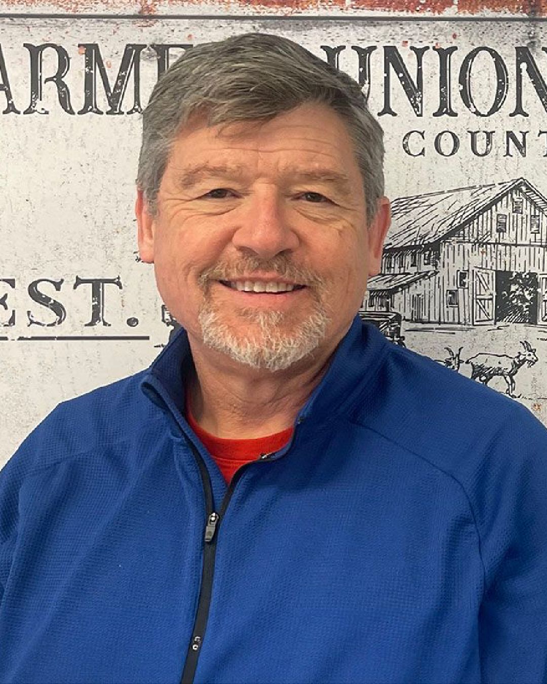 Lyle, agent, in a blue jacket is smiling in front of a sign.
