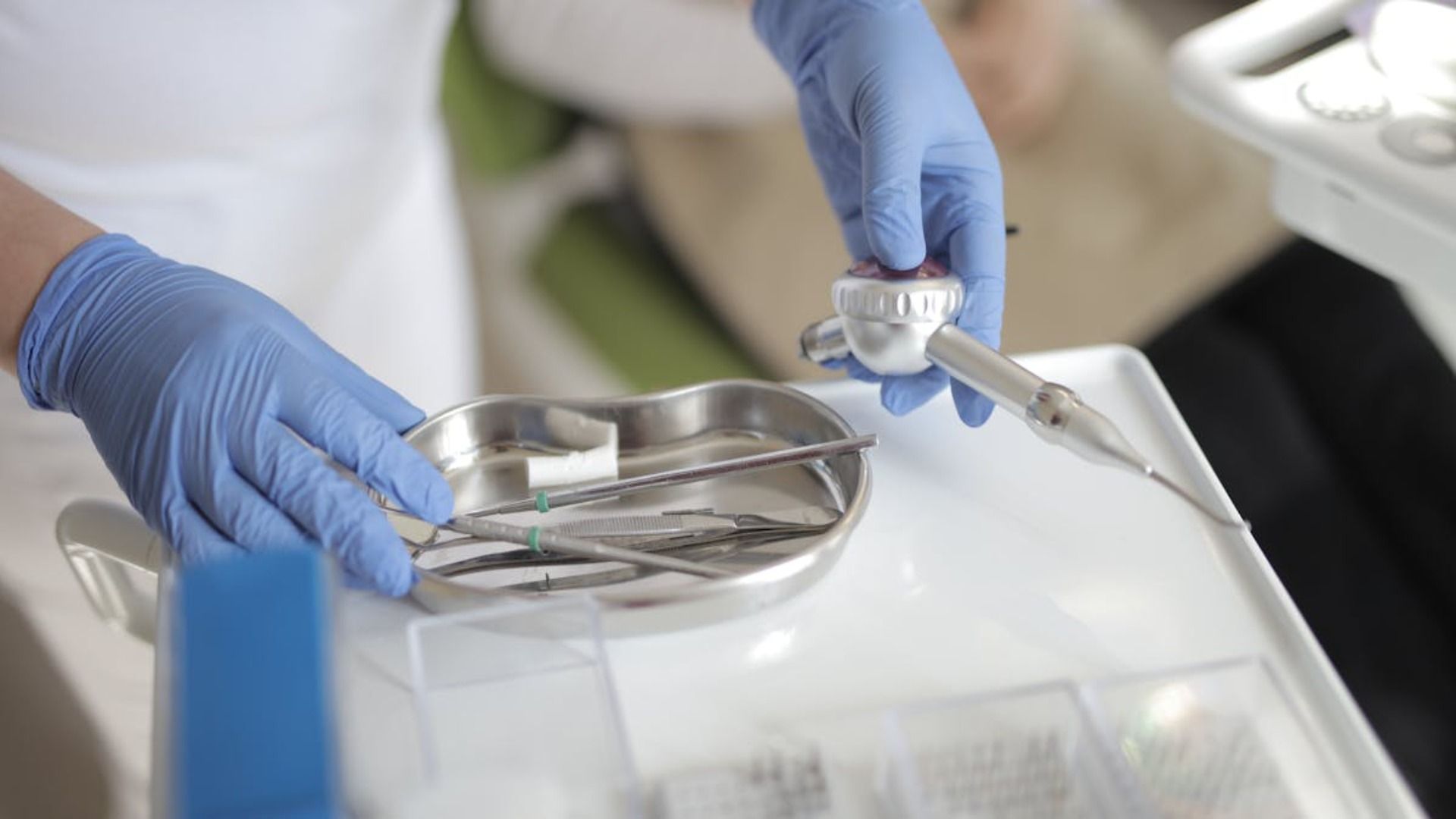 Las manos enguantadas de un dentista seleccionan herramientas de una bandeja junto a un paciente