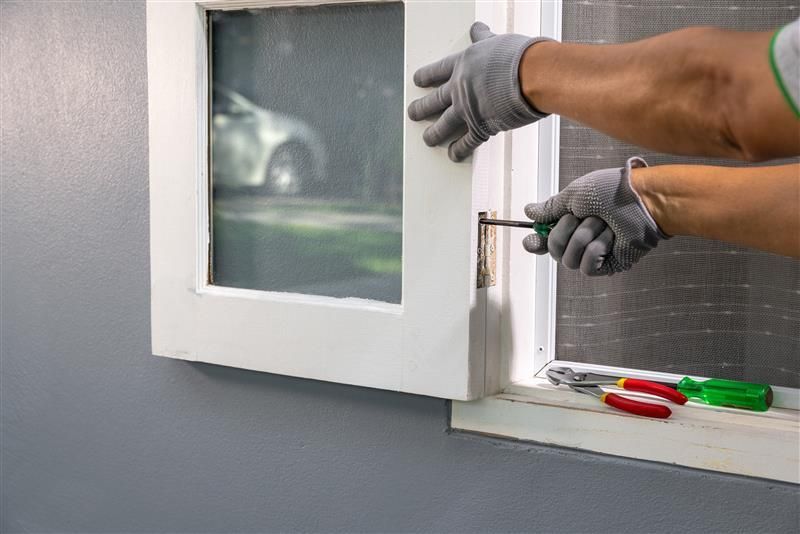 Person with gloves using a screwdriver to adjust a window frame.