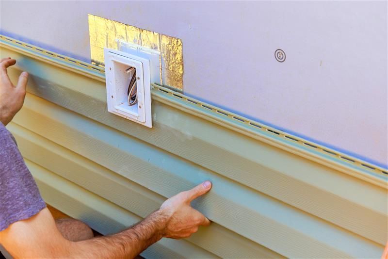 Person installing green vinyl siding on a light purple wall, near a vent.