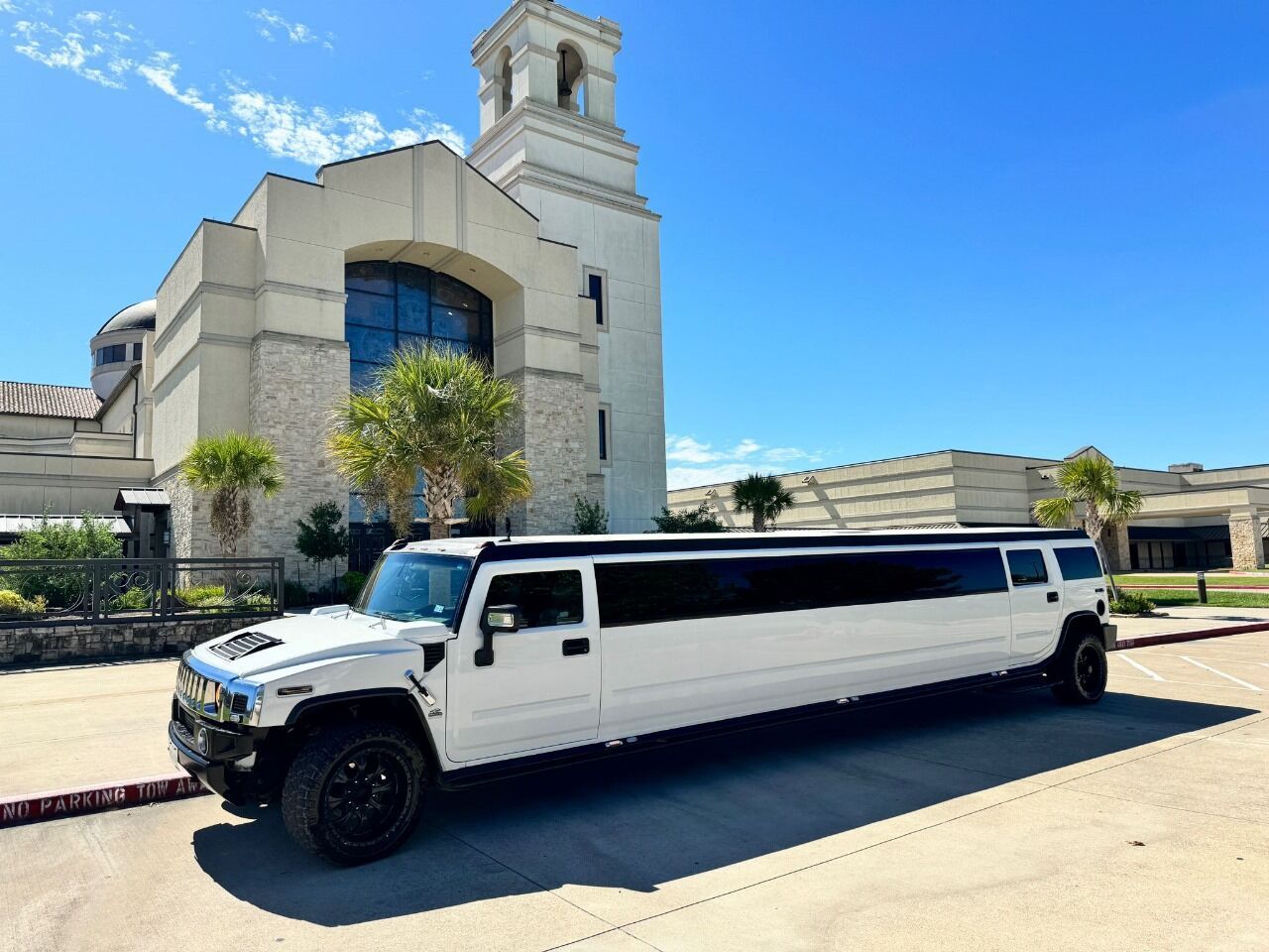 A white hummer limousine is parked in front of a church.