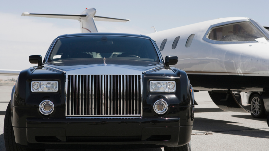 A man in a suit and tie is standing in front of a row of cars.