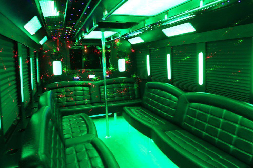 The inside of a limousine with green lights and a pole.