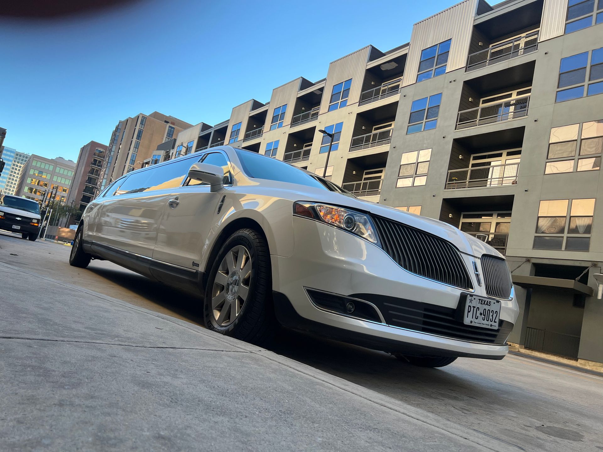 A white limousine is parked on the side of the road in front of a building.