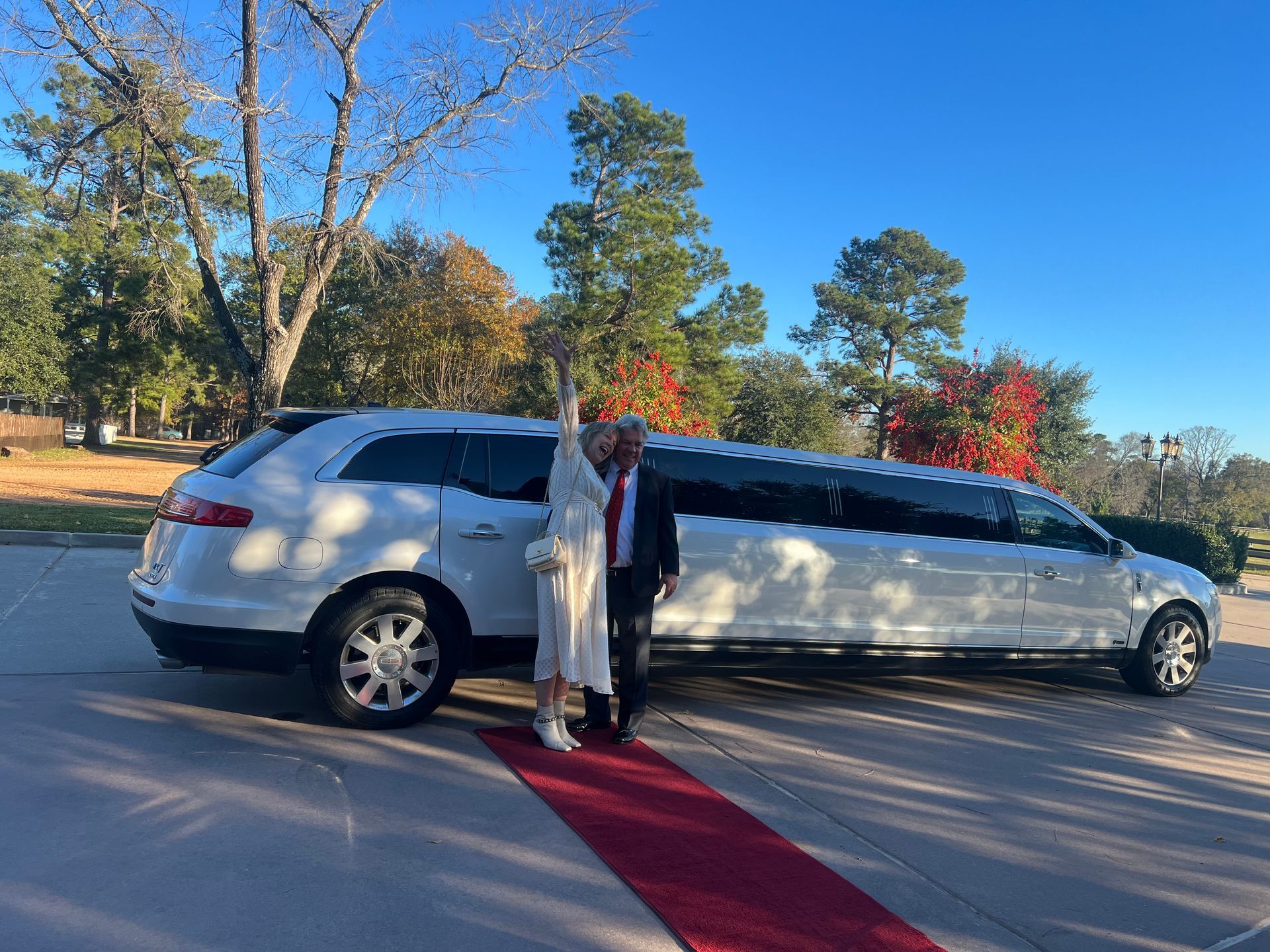 A man and woman are standing in front of a white limousine on a red carpet.