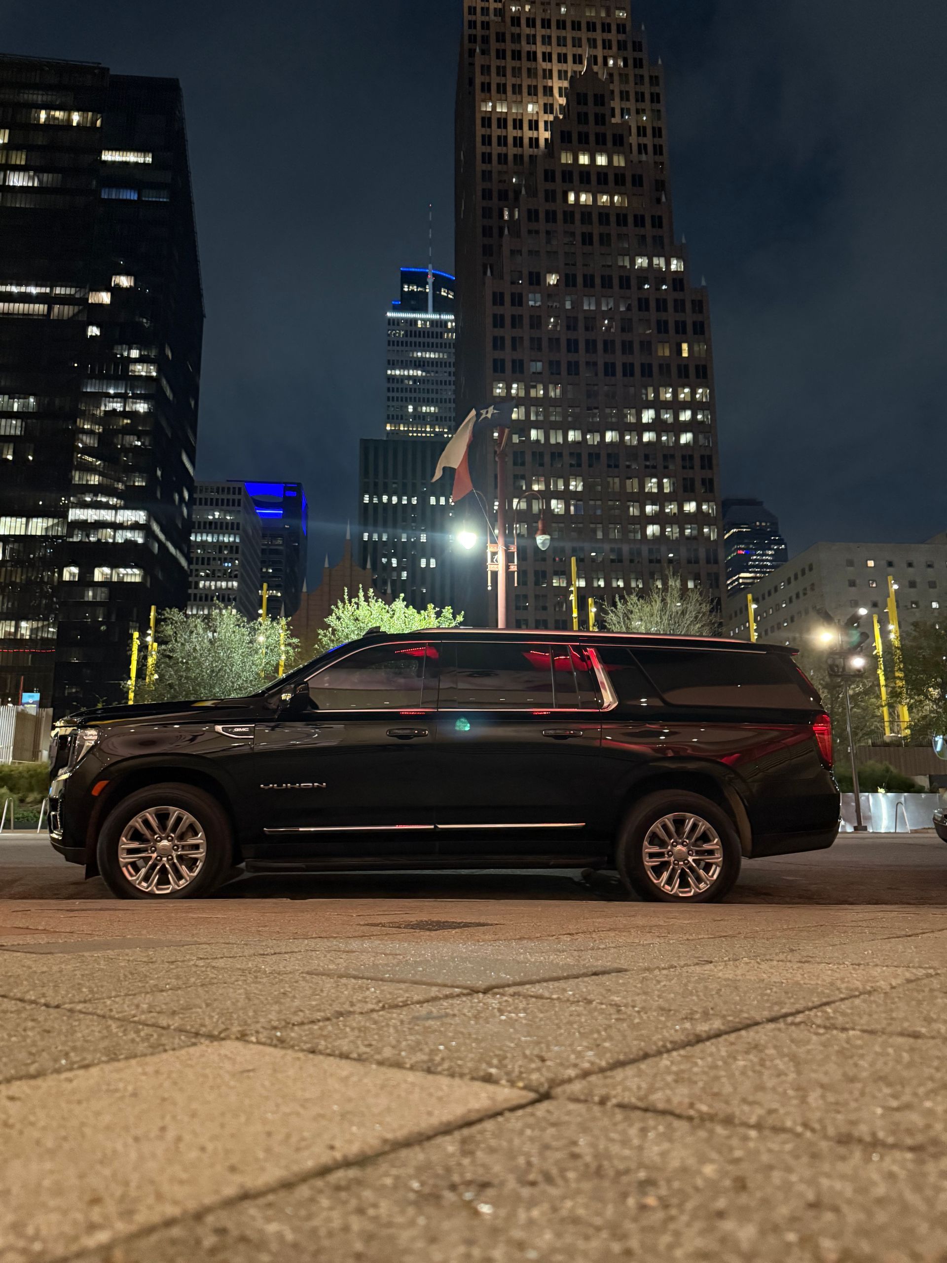 A black suv is parked in front of a city skyline at night.