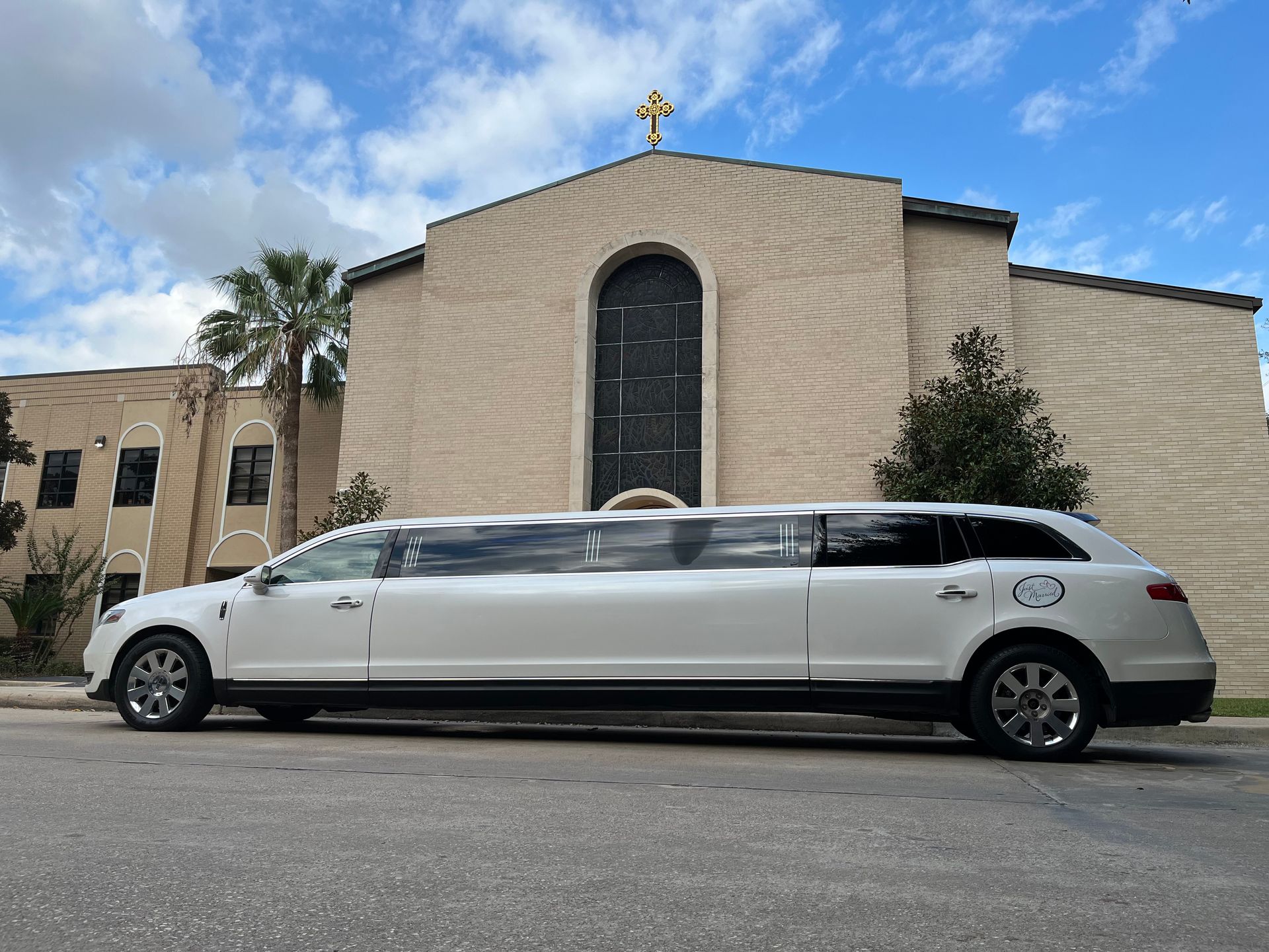 A white limousine is parked in front of a church.