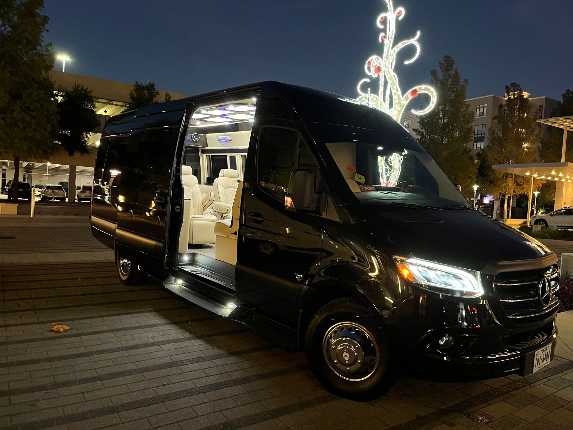 A black van is parked in front of a christmas tree at night.