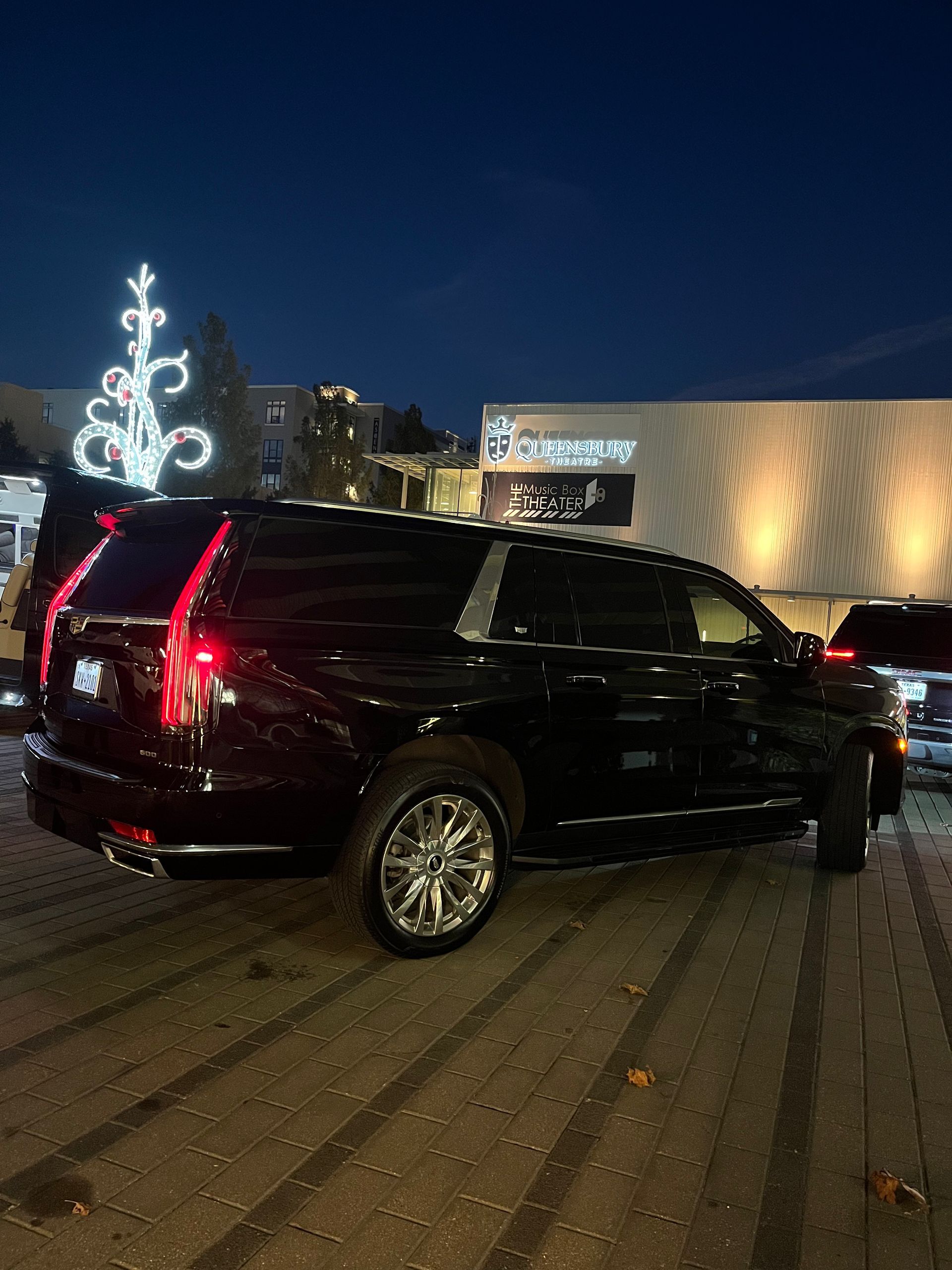 A black suv is parked in a parking lot with a christmas tree in the background.