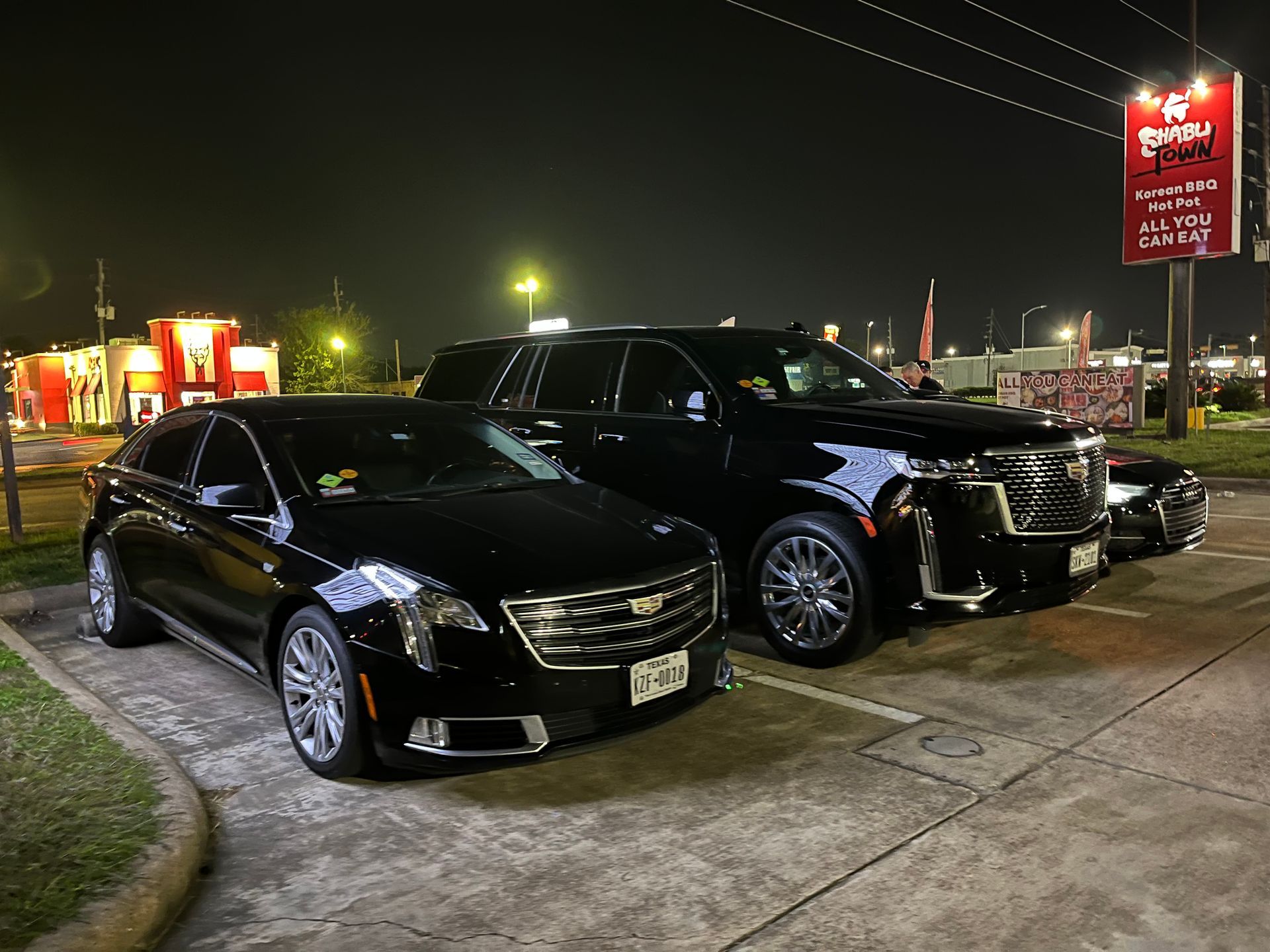 Two black cars are parked in a parking lot at night.
