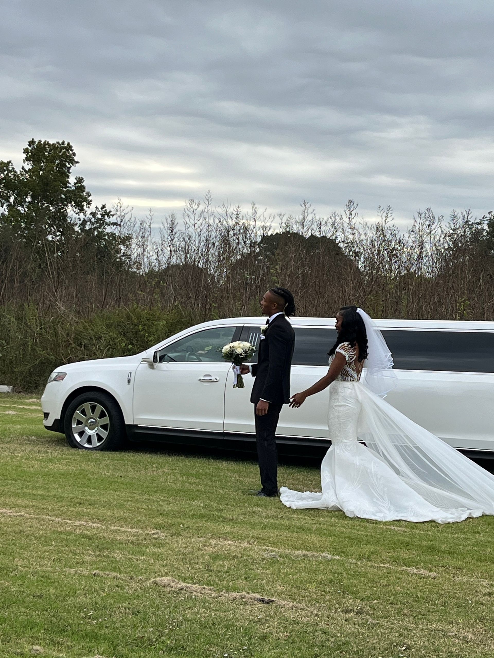 A bride and groom are holding hands in front of a white limousine.