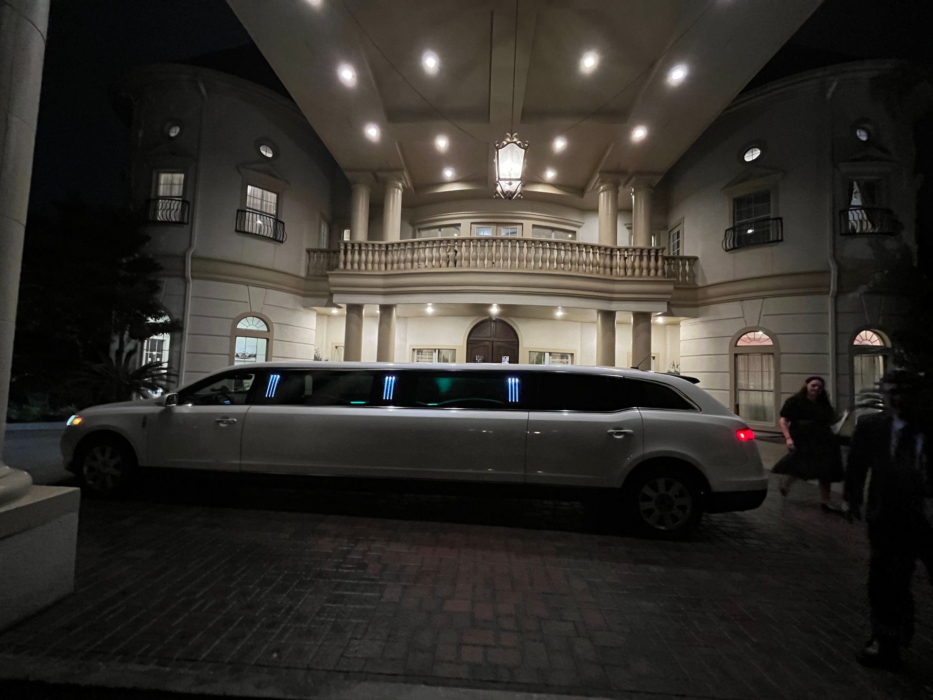 A white limousine is parked in front of a large building at night.