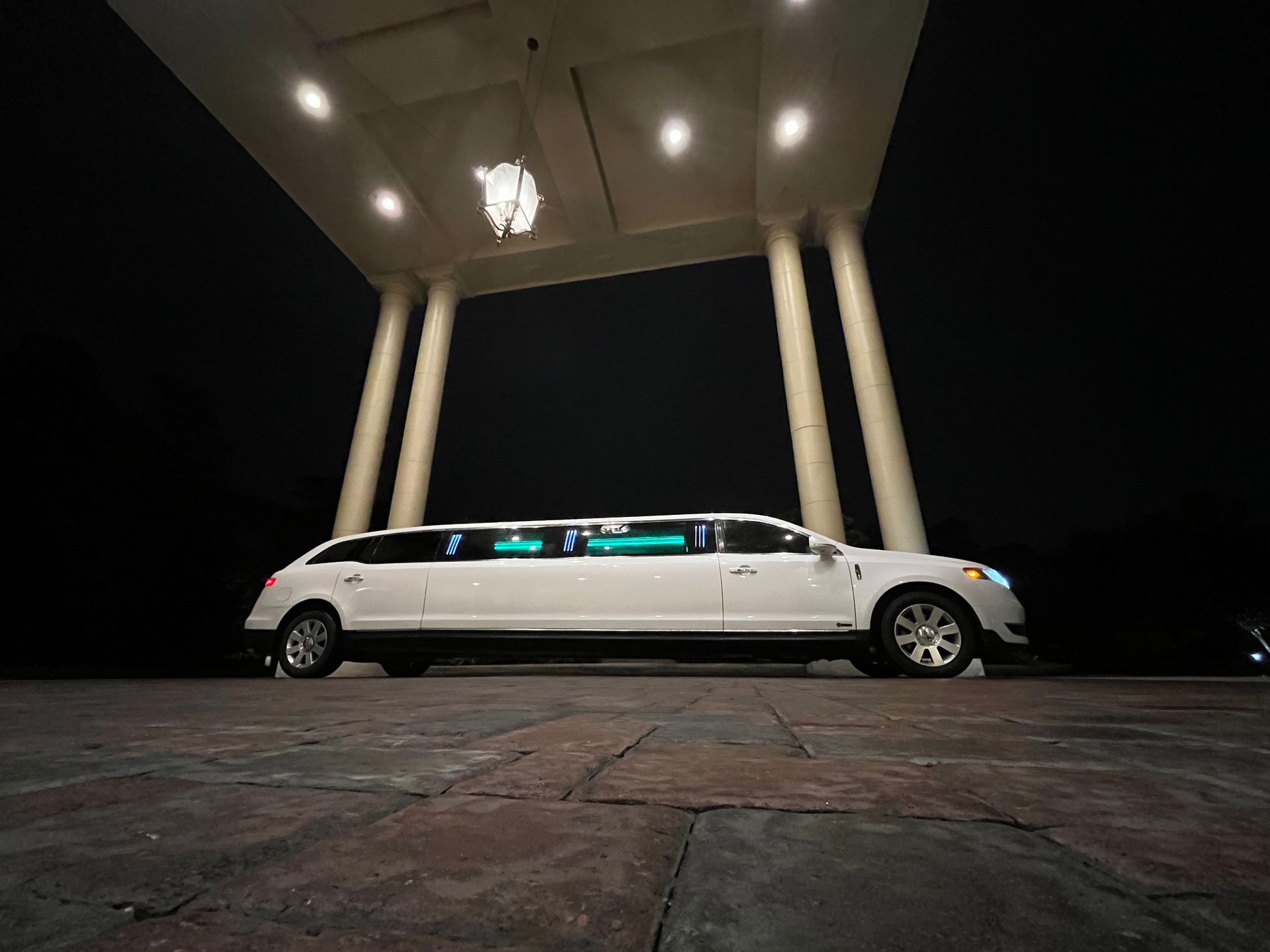 A white limousine is parked in front of a building at night.