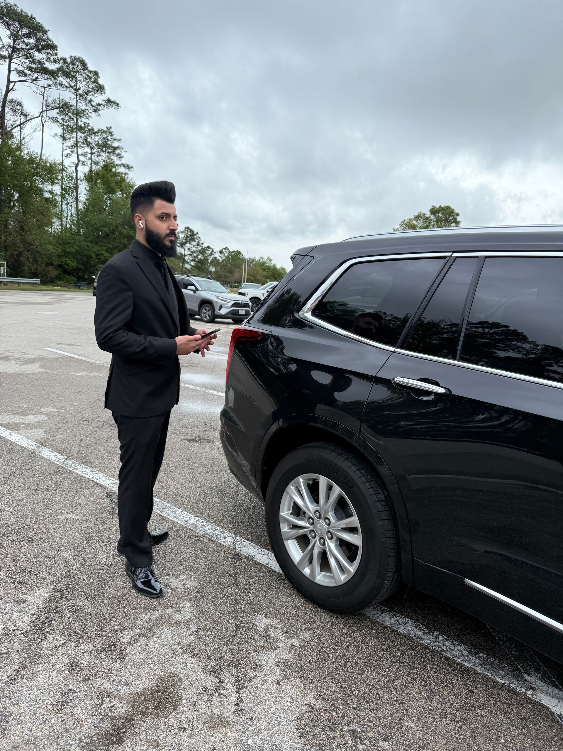 A man in a suit is standing in front of a black suv in a parking lot.