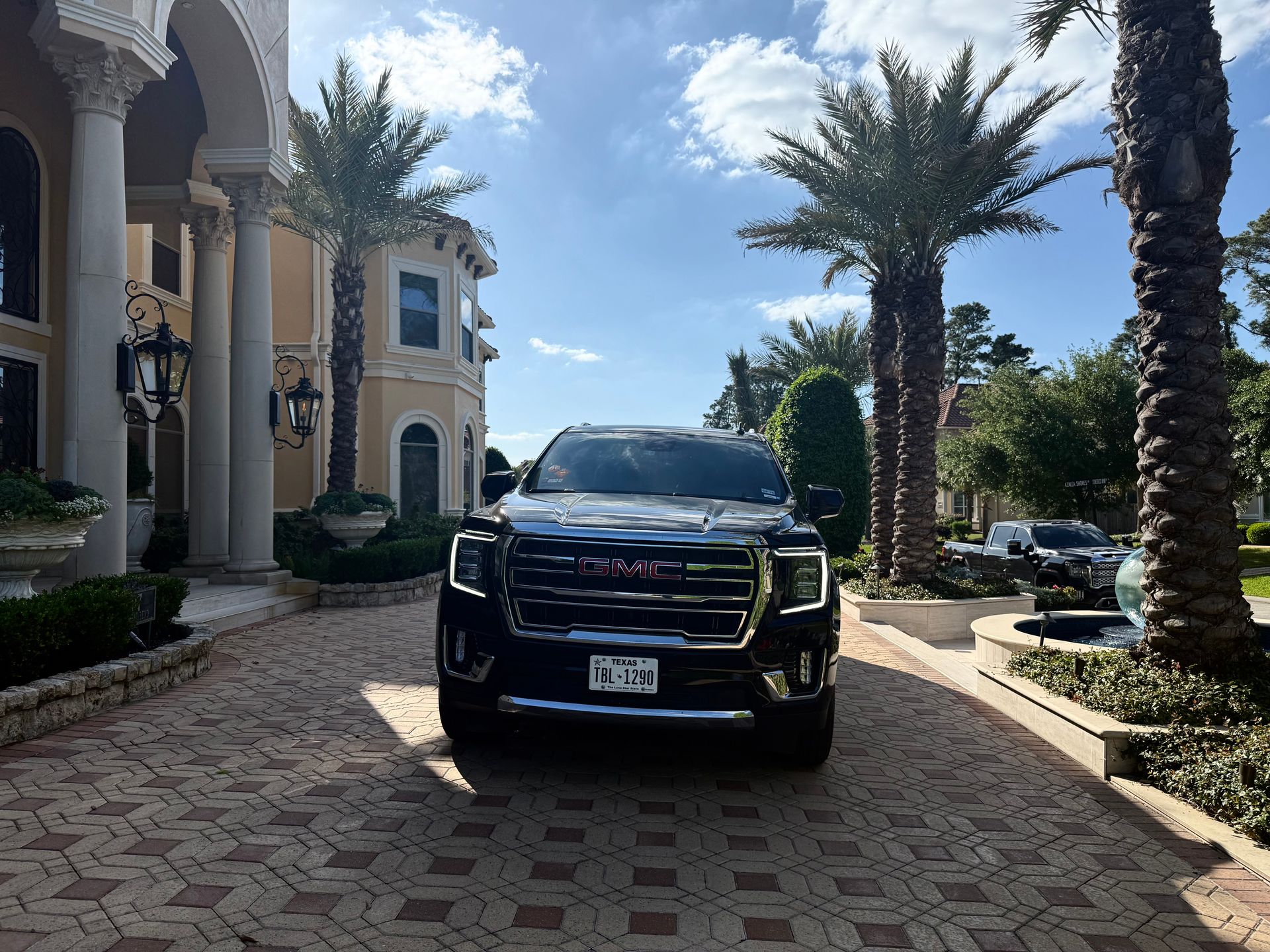 A black gmc truck is parked in front of a large house with palm trees.