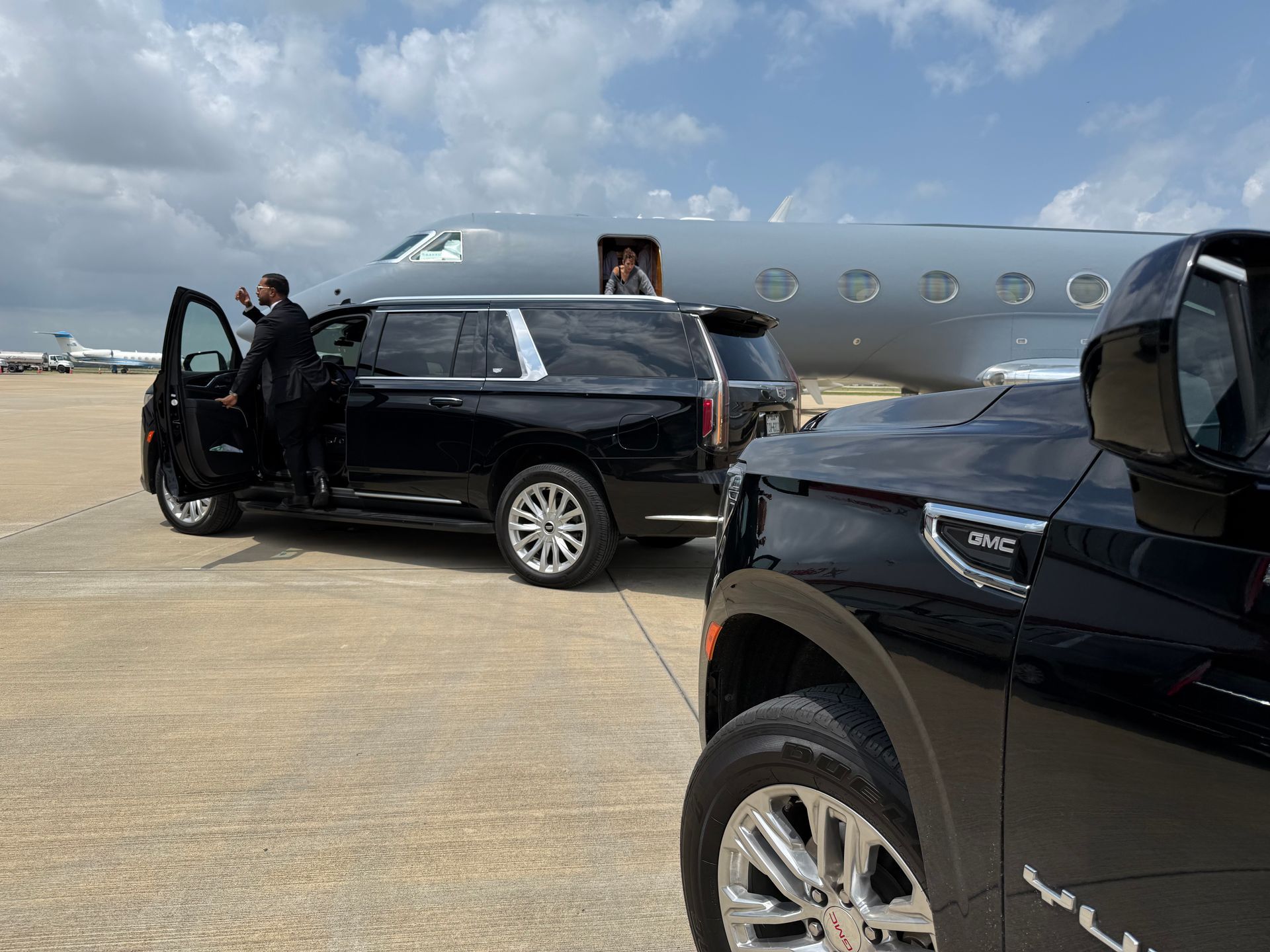 A man is getting out of a black suv next to a private jet.