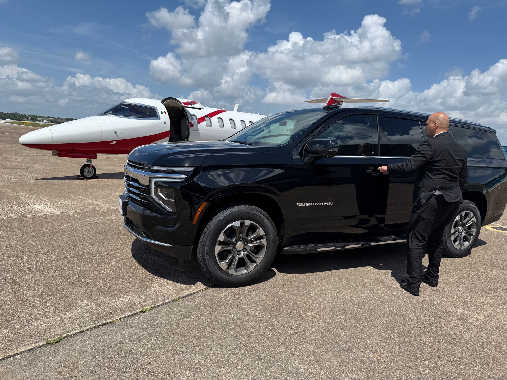 A man is standing next to a black suv in front of a small plane.
