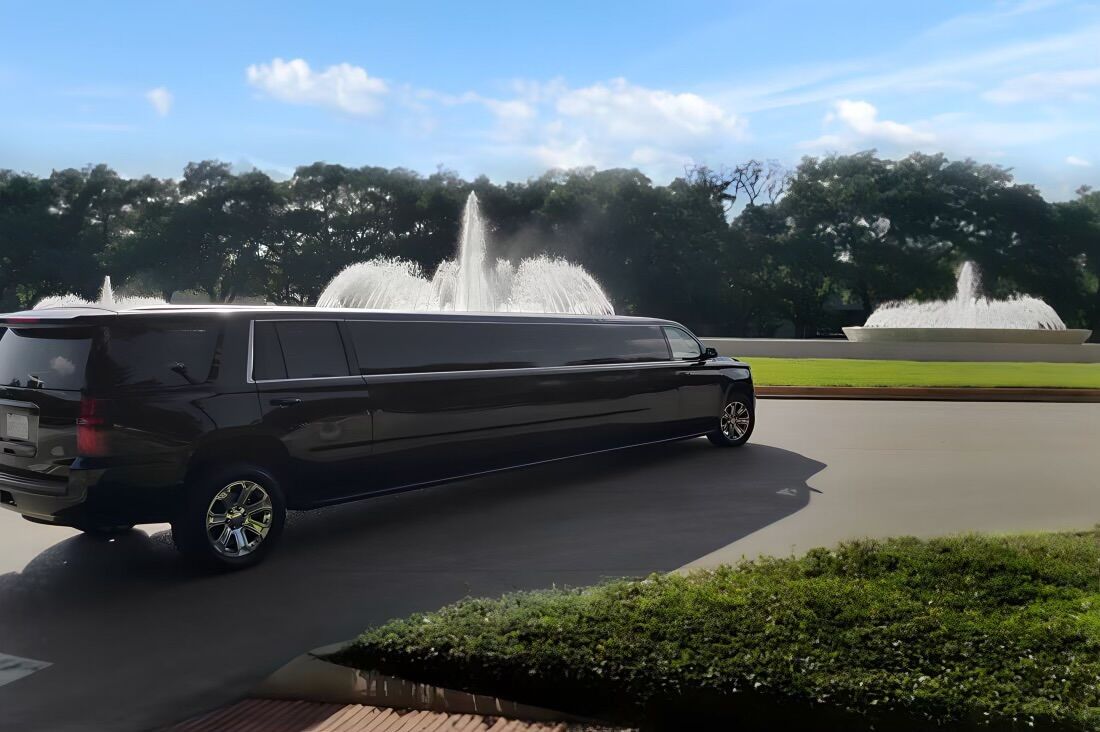 A black limousine is parked in front of a fountain.