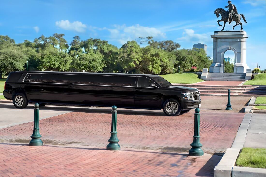 A black limousine is parked in front of a statue of a man on a horse.