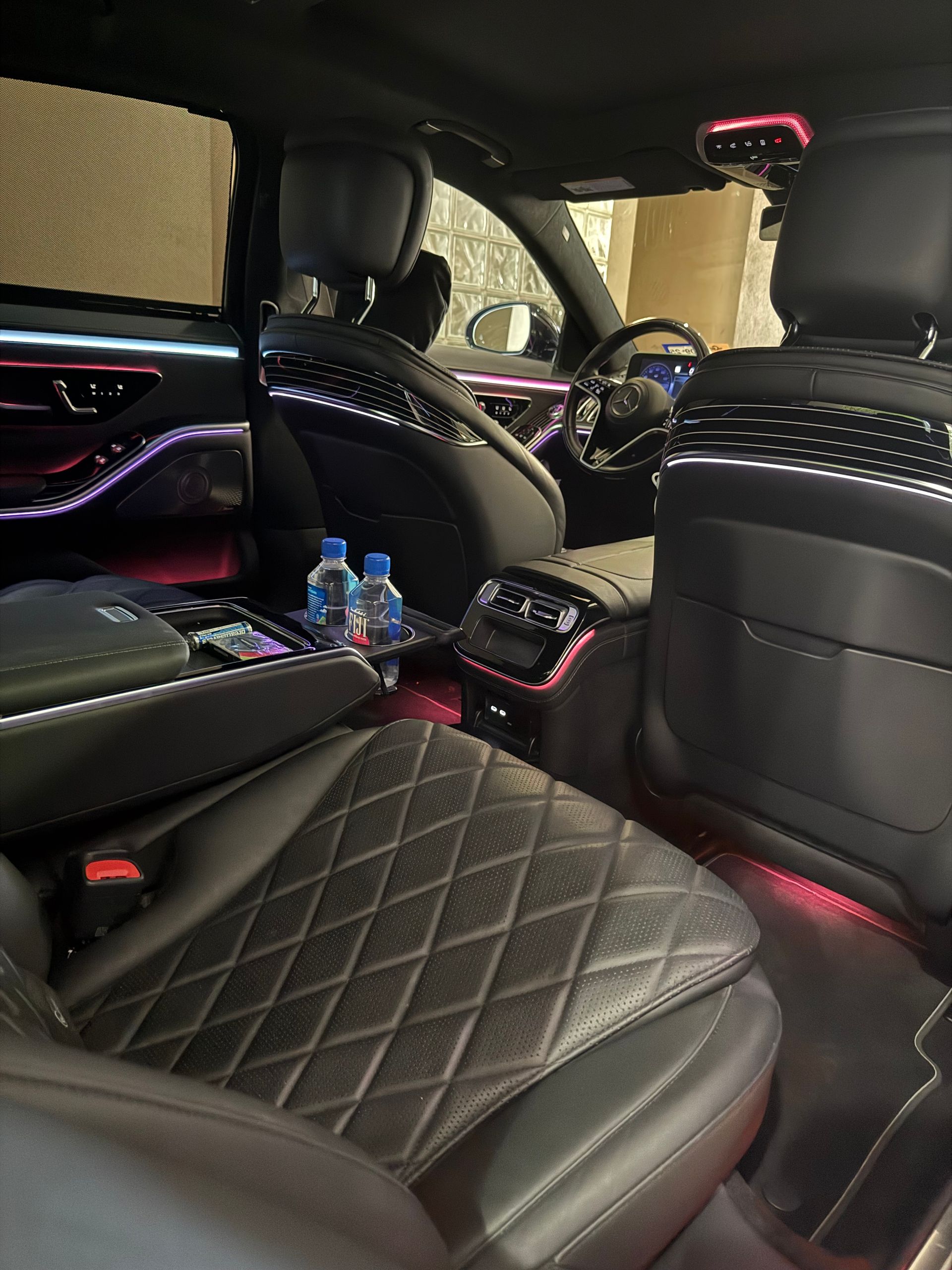 Luxurious car interior: black leather seats, diamond stitching, ambient lighting, water bottles in the center console.