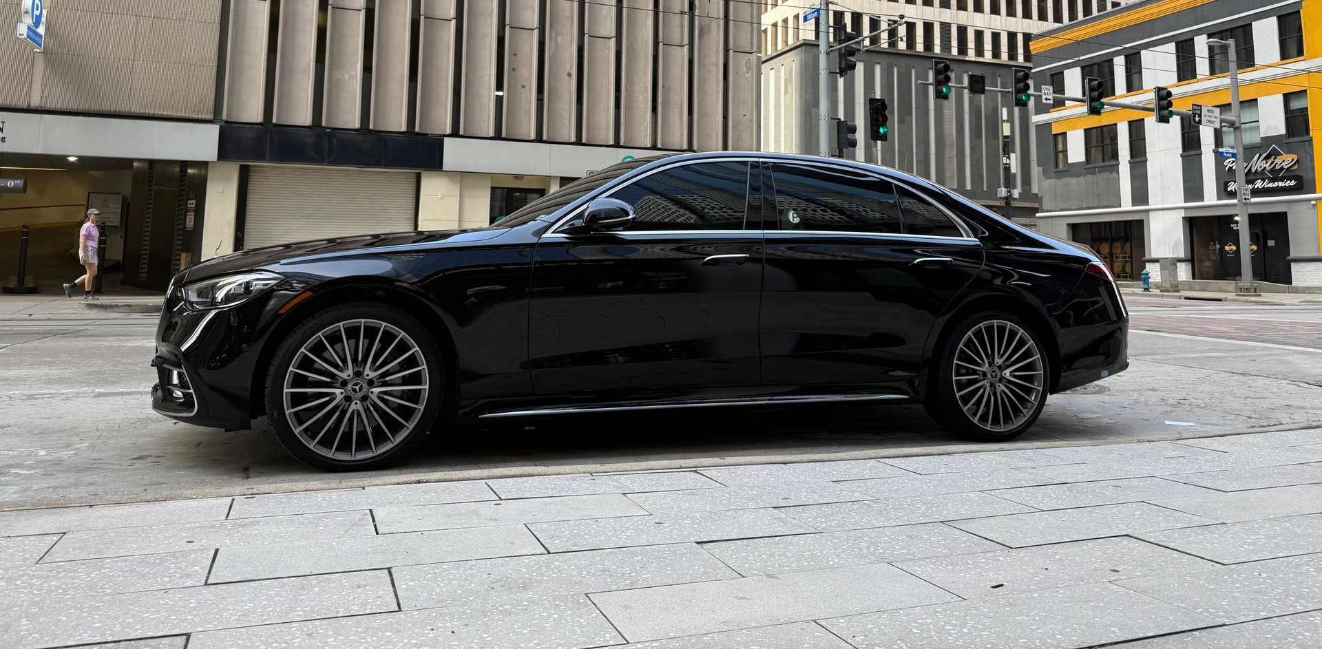 Black Mercedes sedan parked on a city street with buildings in the background.