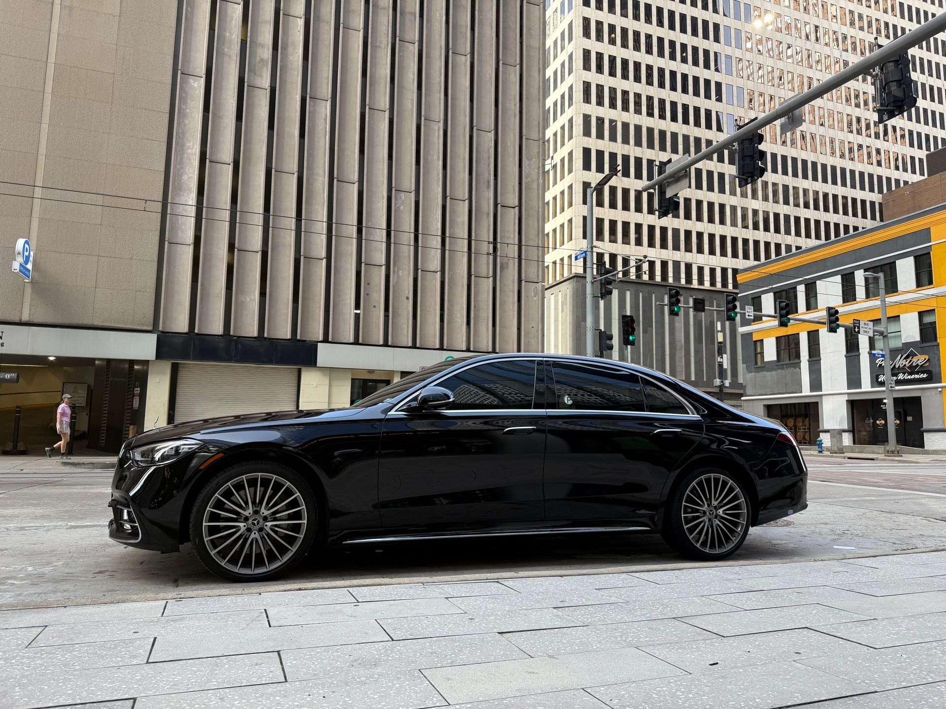 Black Mercedes sedan parked on a city street, tall buildings in the background.
