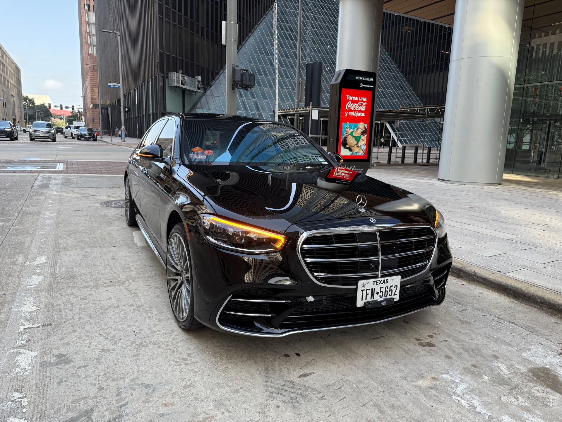 Black Mercedes sedan parked on a city street with modern buildings in the background.
